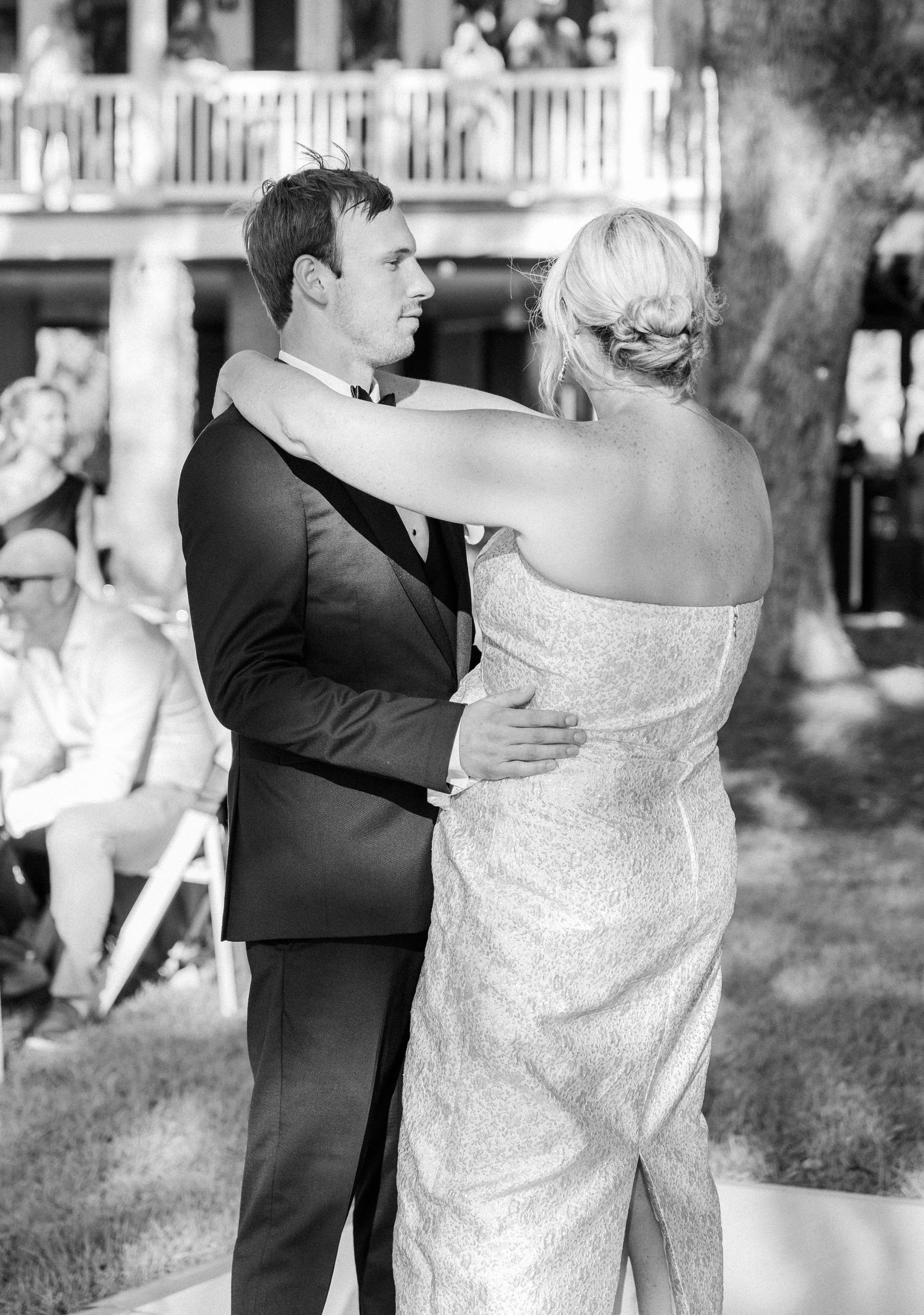 Groom smiles at bride during outdoor wedding ceremony with guests seated in background.