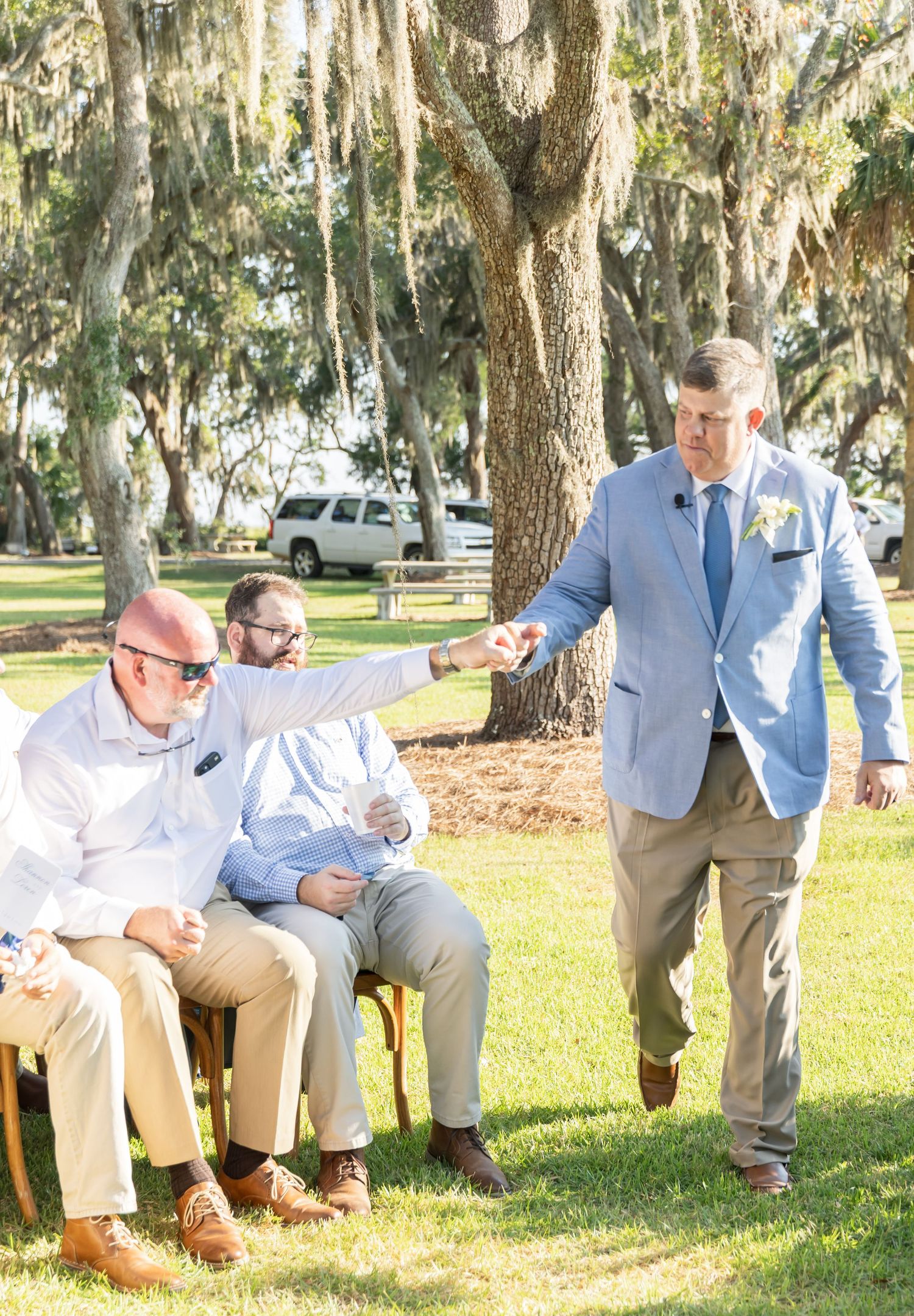 A group sits on a fallen tree trunk in a park with Spanish moss draped oak trees in the background.