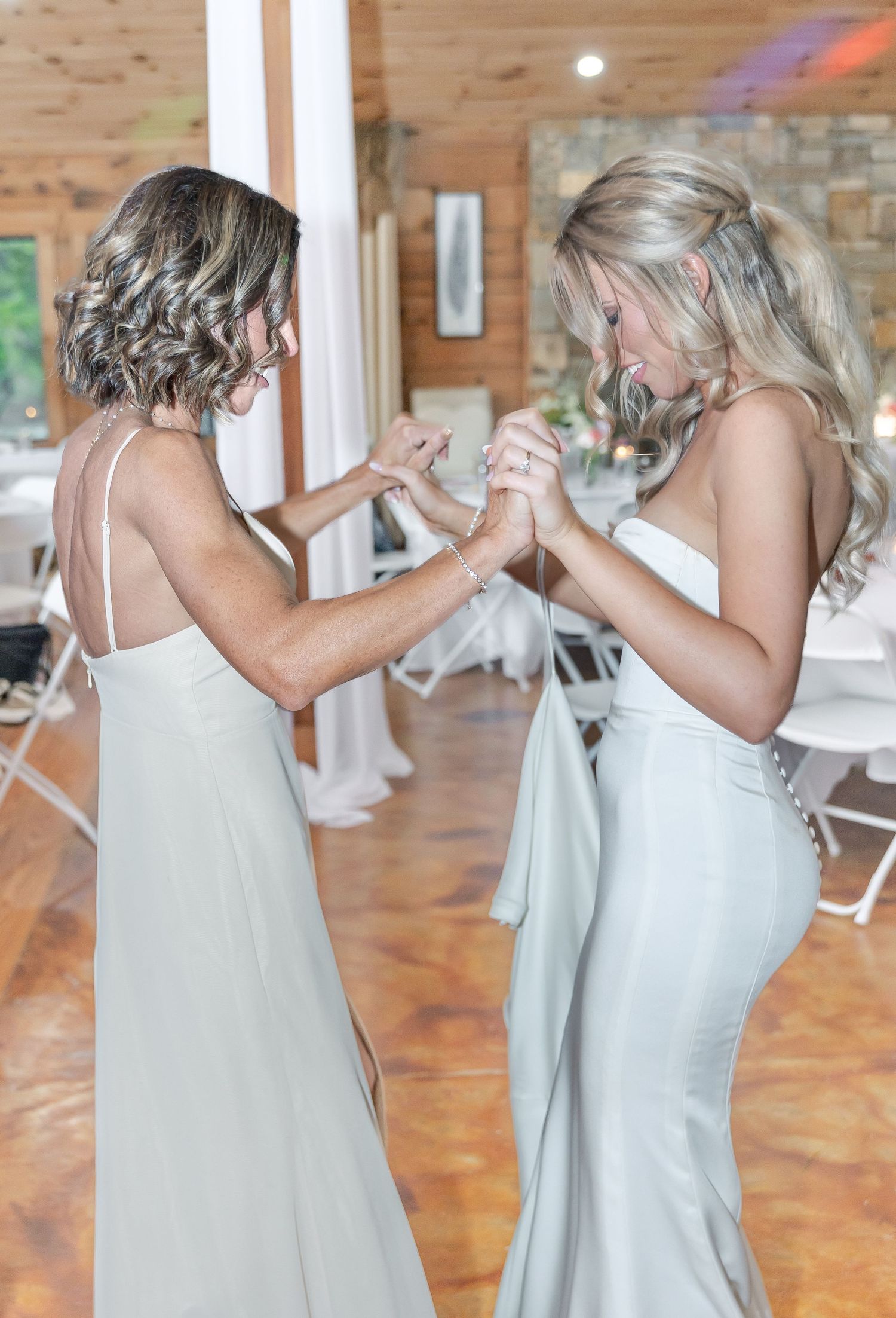 Friends in matching silver dresses dancing and holding hands at a wedding celebration.