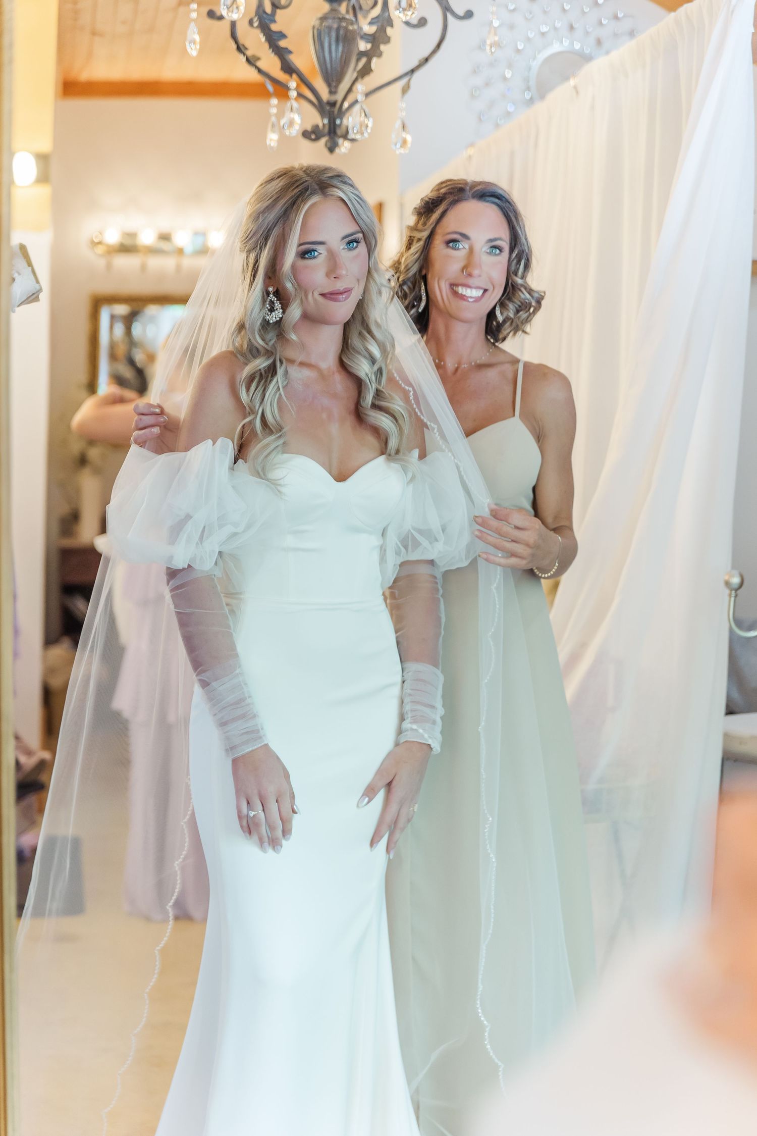 Elegant bridal showcase with fitted white gown and champagne bridesmaid dress in rustic setting.