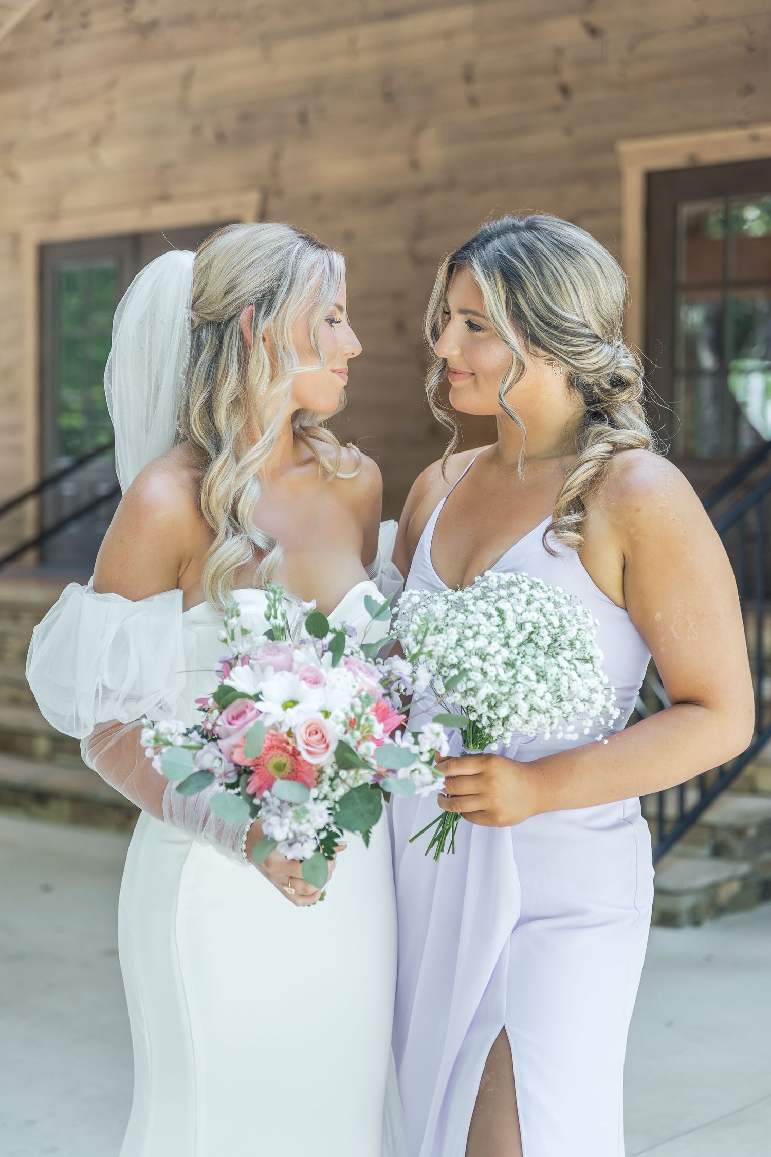 Two women in elegant wedding attire share an intimate moment while holding baby's breath and floral bouquets.