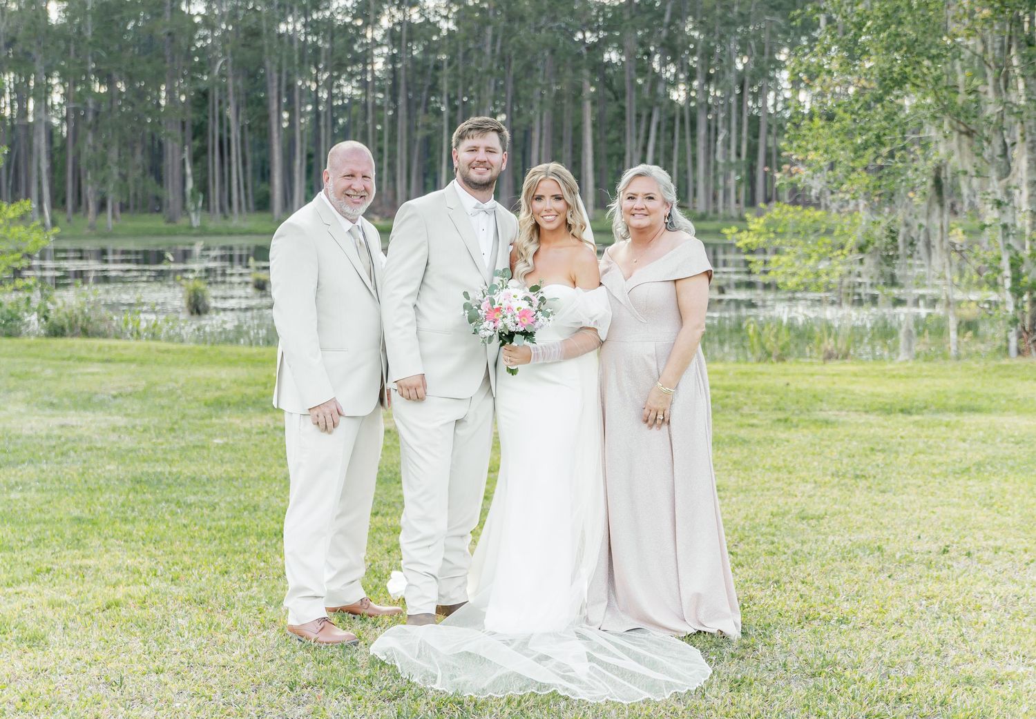 Elegant wedding group photo with everyone dressed in white against a natural forest backdrop.