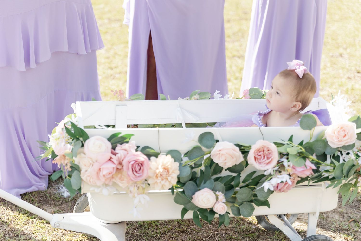 Decorated white wagon with pink roses and eucalyptus against lavender fabric backdrop.