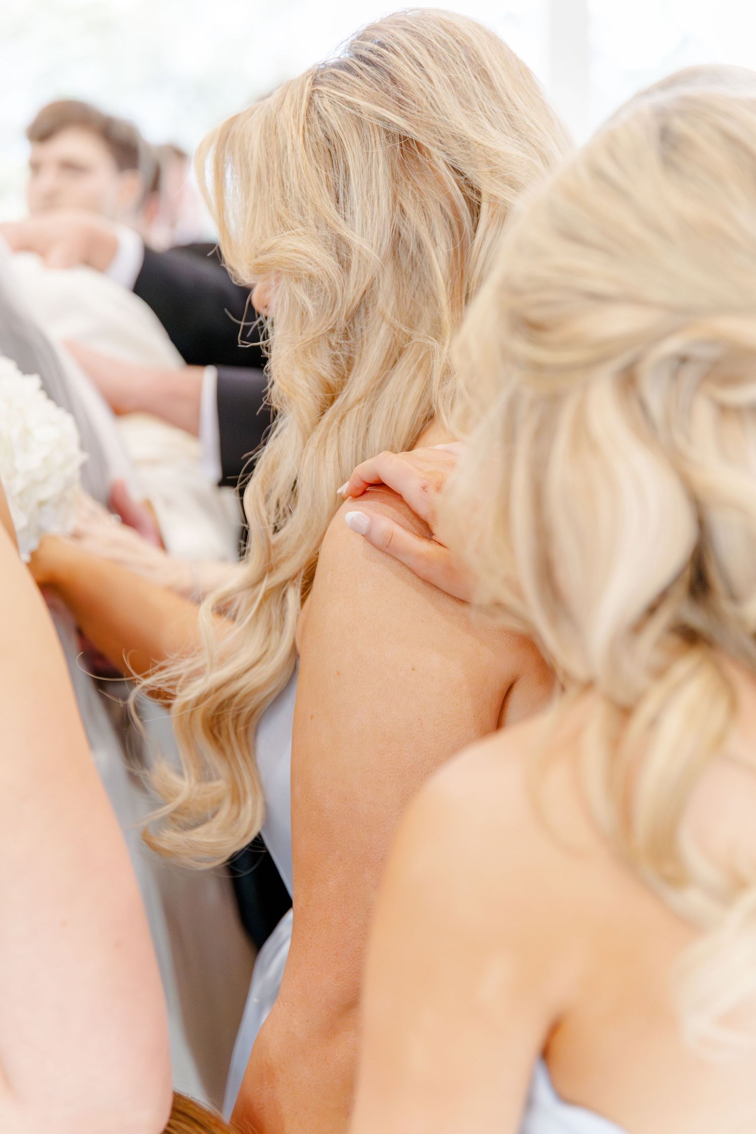 Close-up of blonde wedding guests holding hands in support during emotional outdoor wedding ceremony.