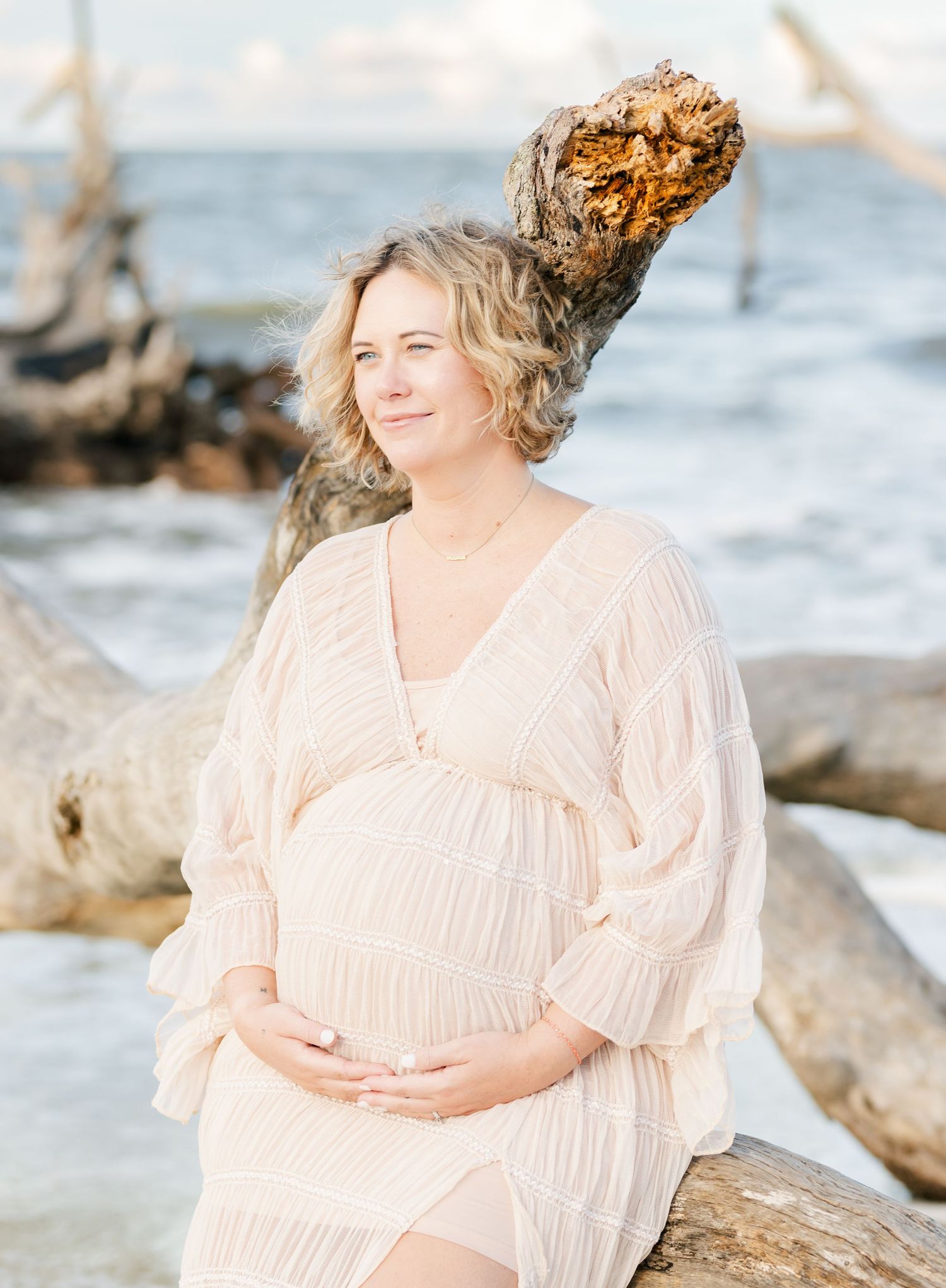 Peaceful maternity portraits by the ocean featuring driftwood and waves.