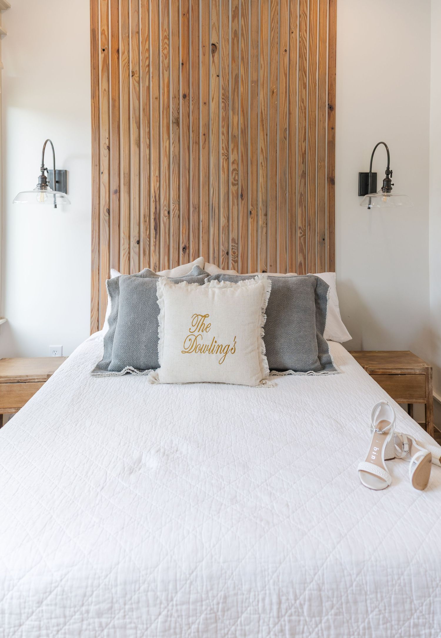 Elegant wedding bedroom with wood slat headboard, white bedding, gray pillows, and personalized The Dowlings throw pillow.