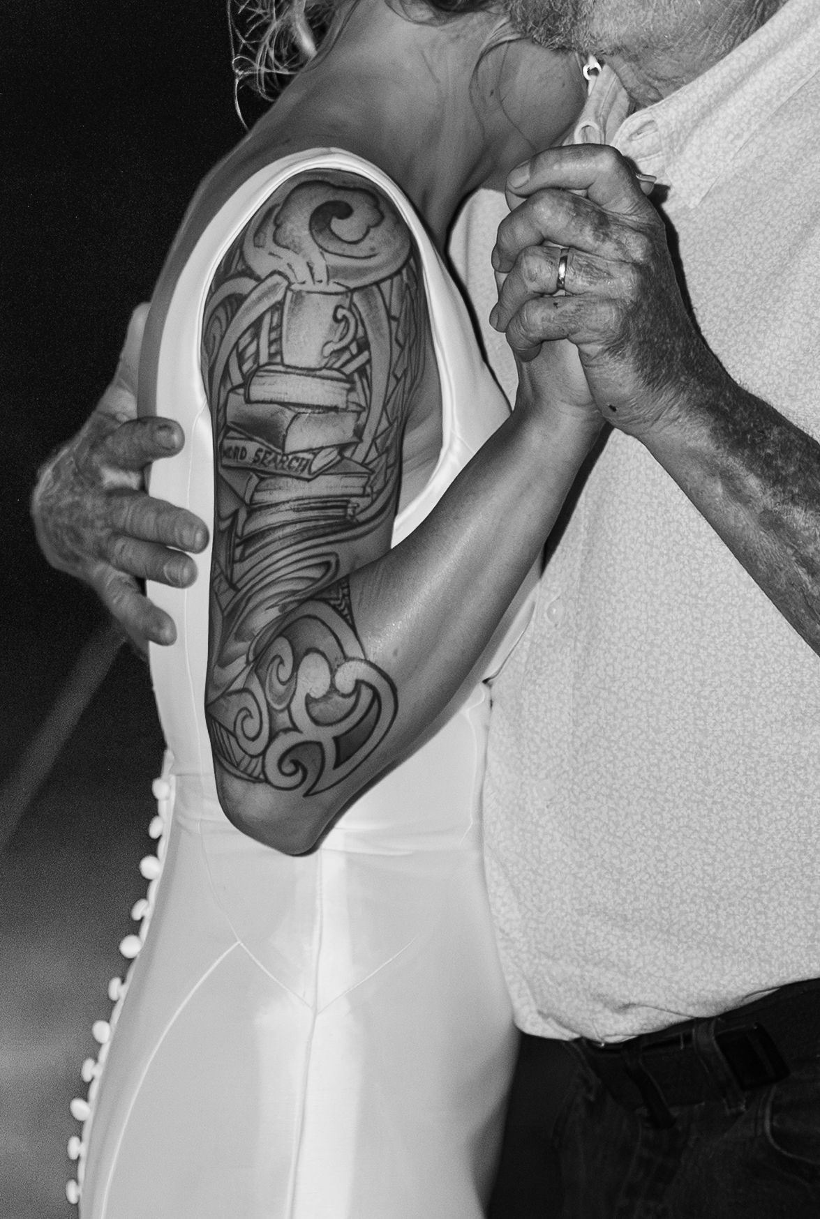 Black and white close-up of bride with detailed sleeve tattoo dancing with partner at reception.