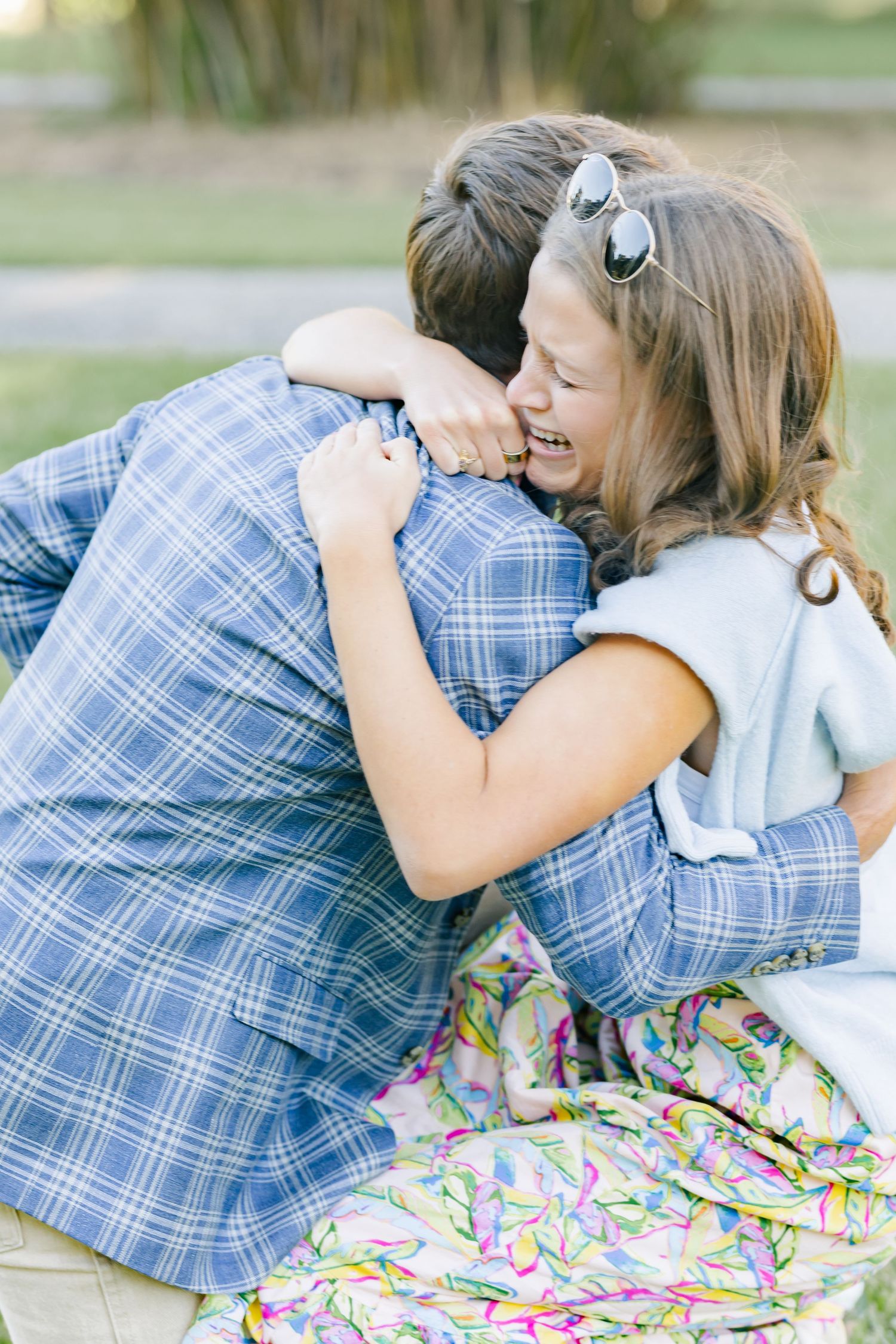 Two people share a joyful embrace outdoors, wearing blue plaid and floral patterns.