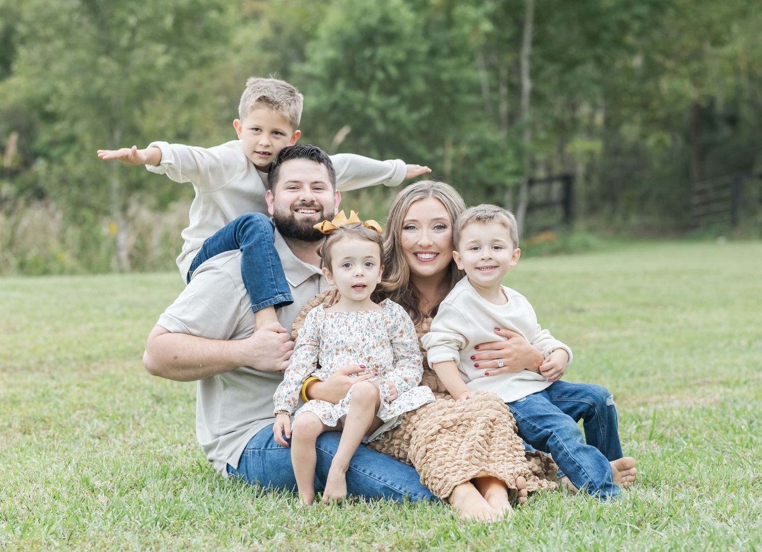 A family group relaxes together on grassy hillside during an outdoor photo session in a natural setting.