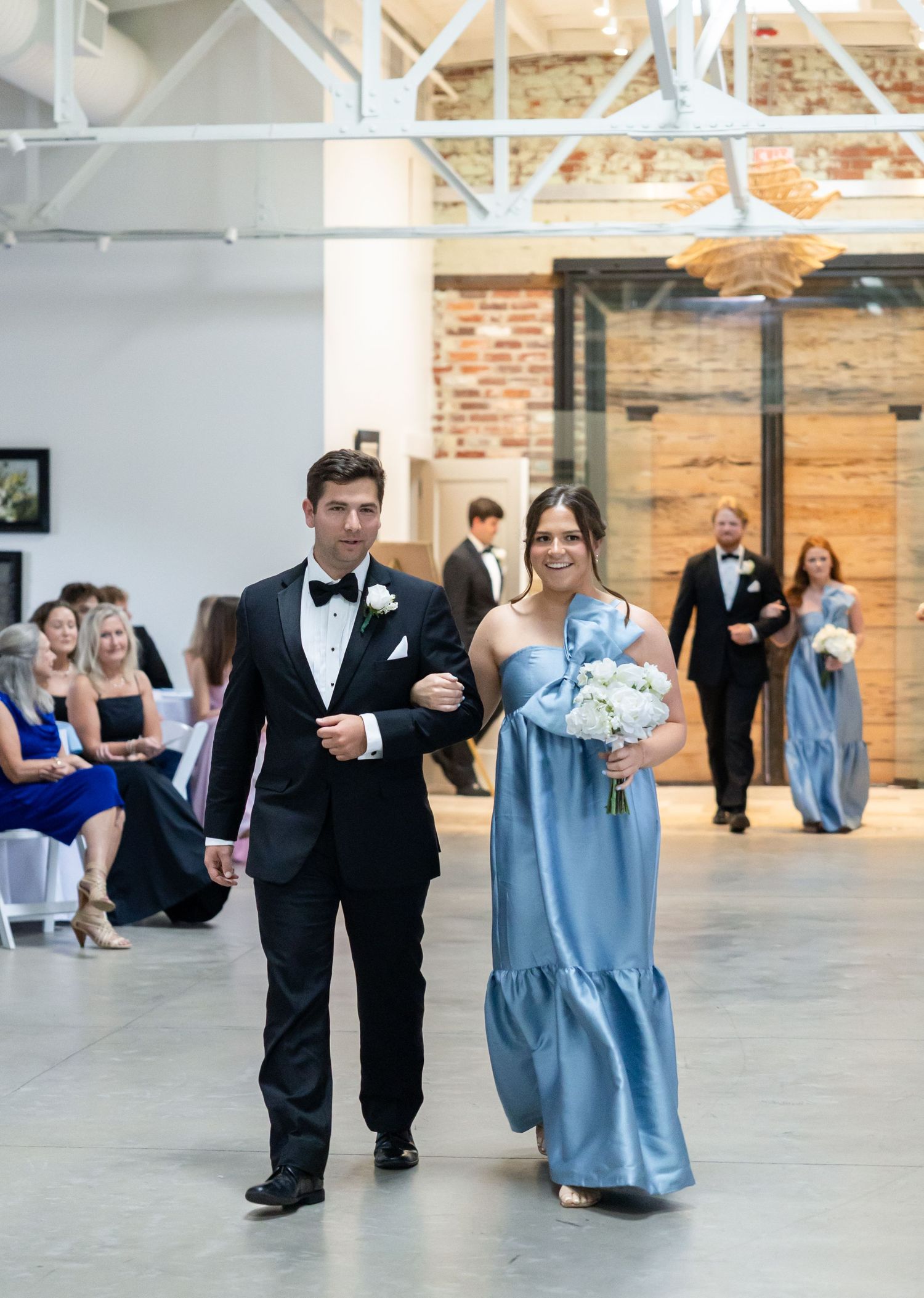 Groomsman escorts bridesmaid in blue satin gown down the aisle during wedding ceremony.