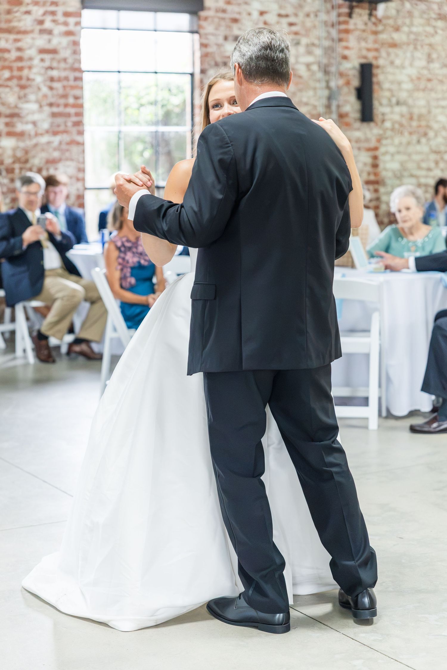 Bride shares an emotional father-daughter dance in a rustic brick-walled reception venue.