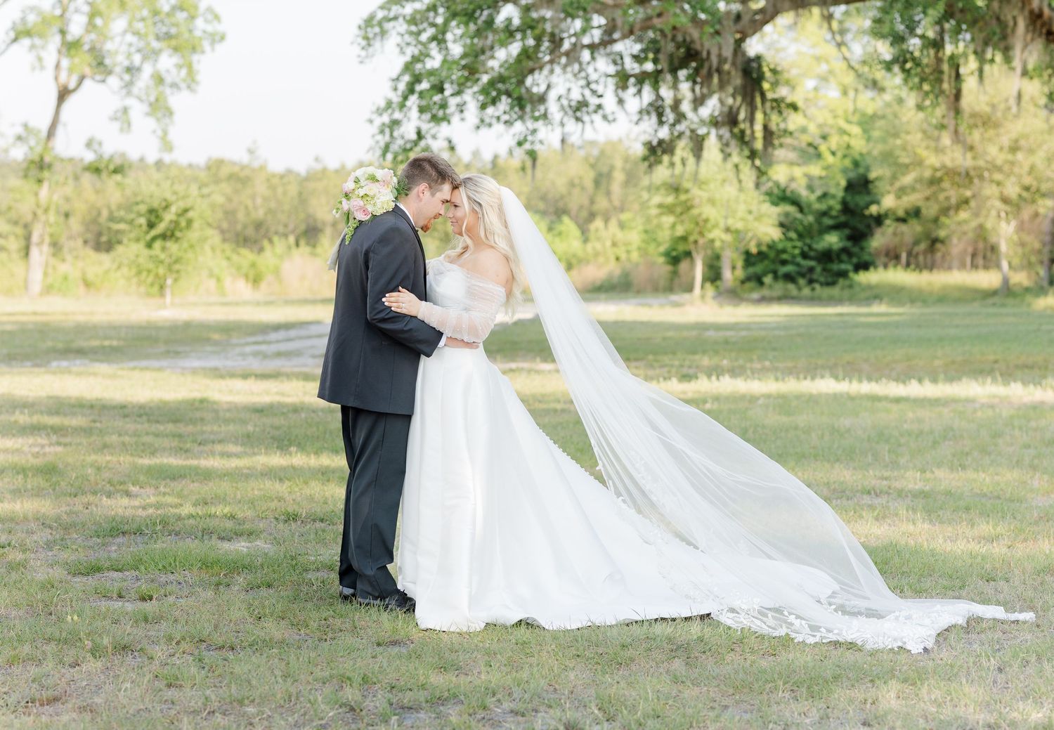 Bride and groom sharing romantic moment outdoors with flowing cathedral veil.