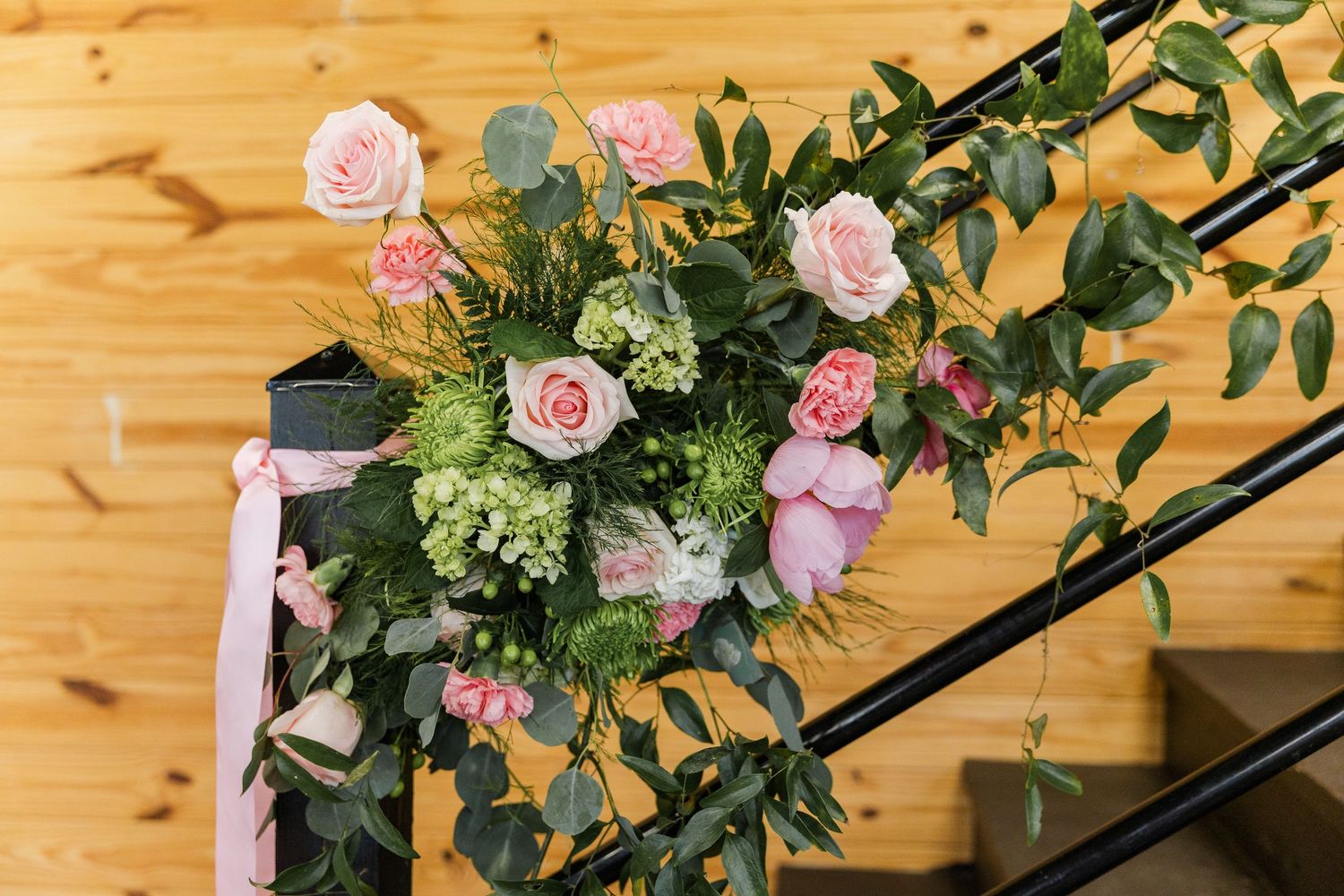Pink roses and greenery floral arrangement decorating black staircase railing at a wedding venue.