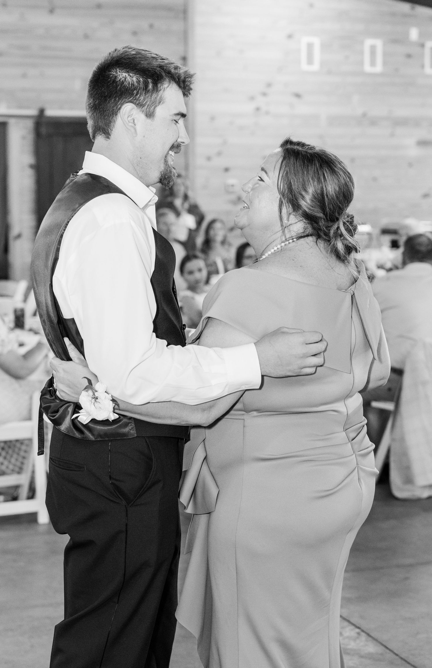Groom smiling while sharing a dance with his mother at a wedding reception in a rustic barn venue.