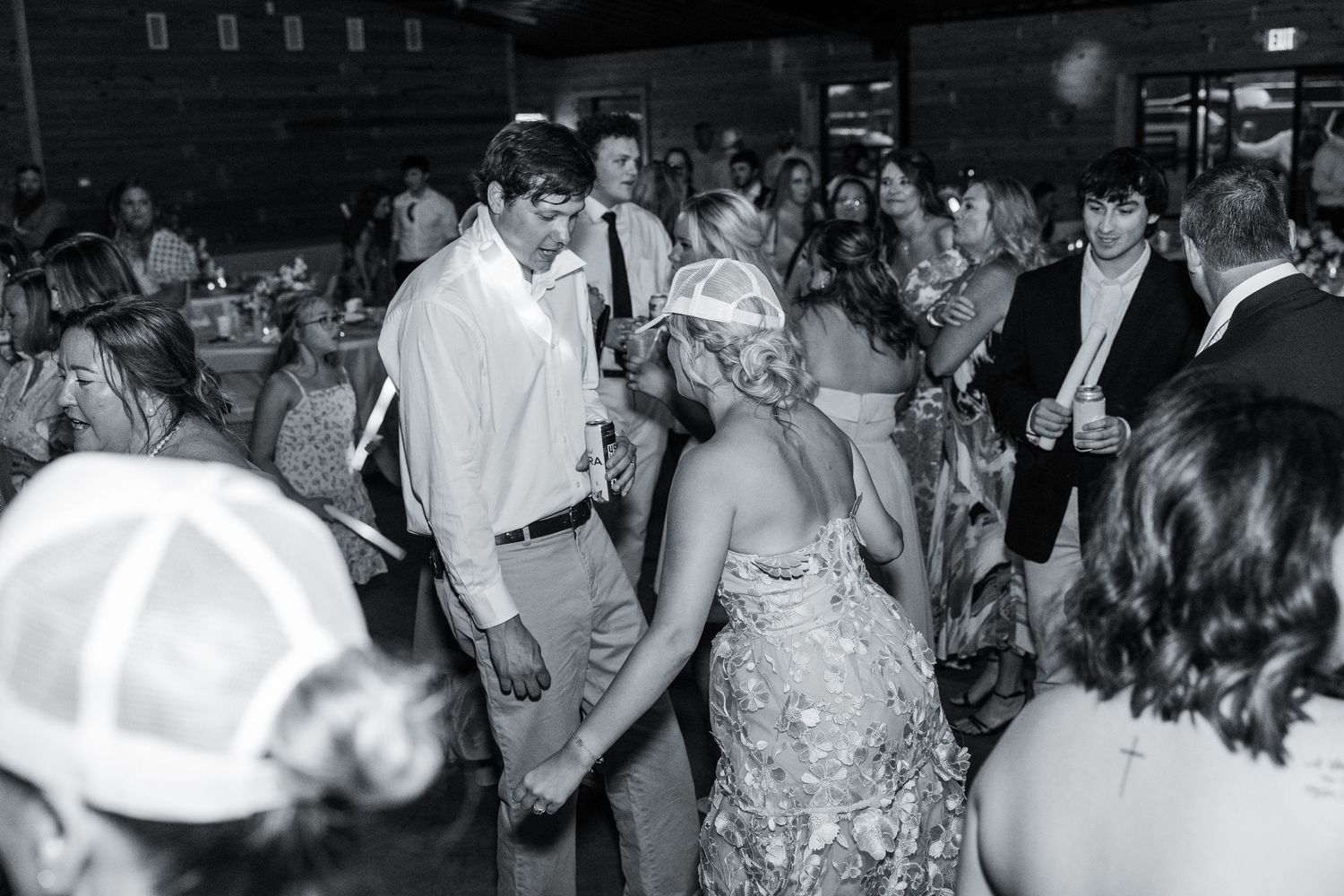 Bride and groom dancing together surrounded by guests at wedding reception in black and white.