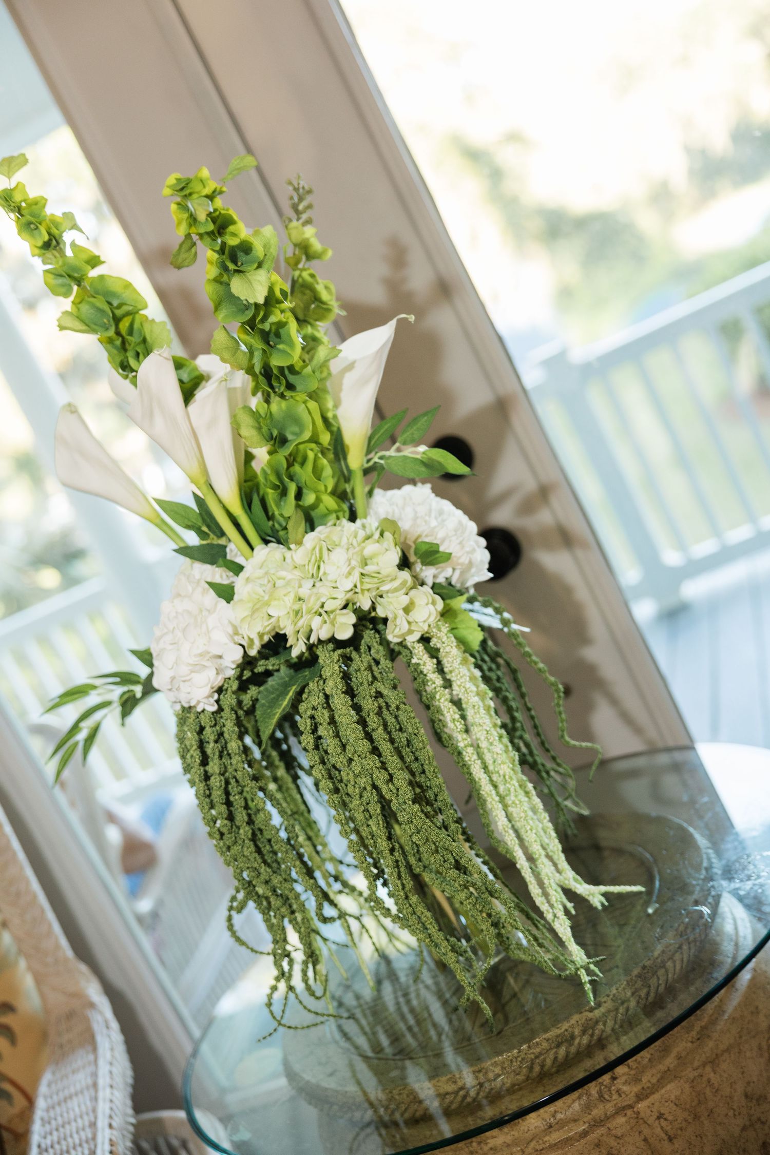 Elegant white and green floral arrangement with calla lilies and cascading amaranthus on a glass table.