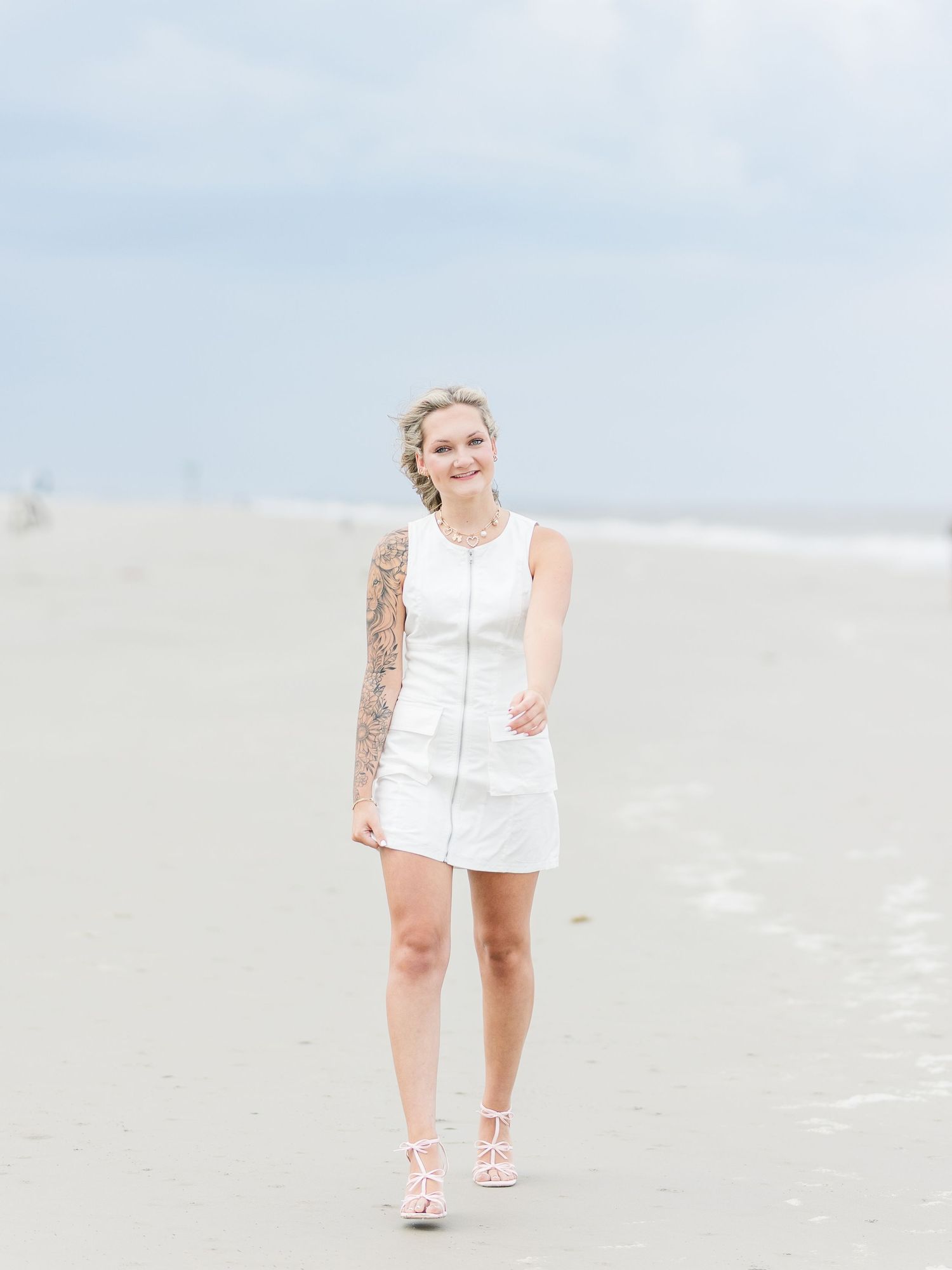 Coastal portrait with white zipper dress and pink sandals on sandy beach.