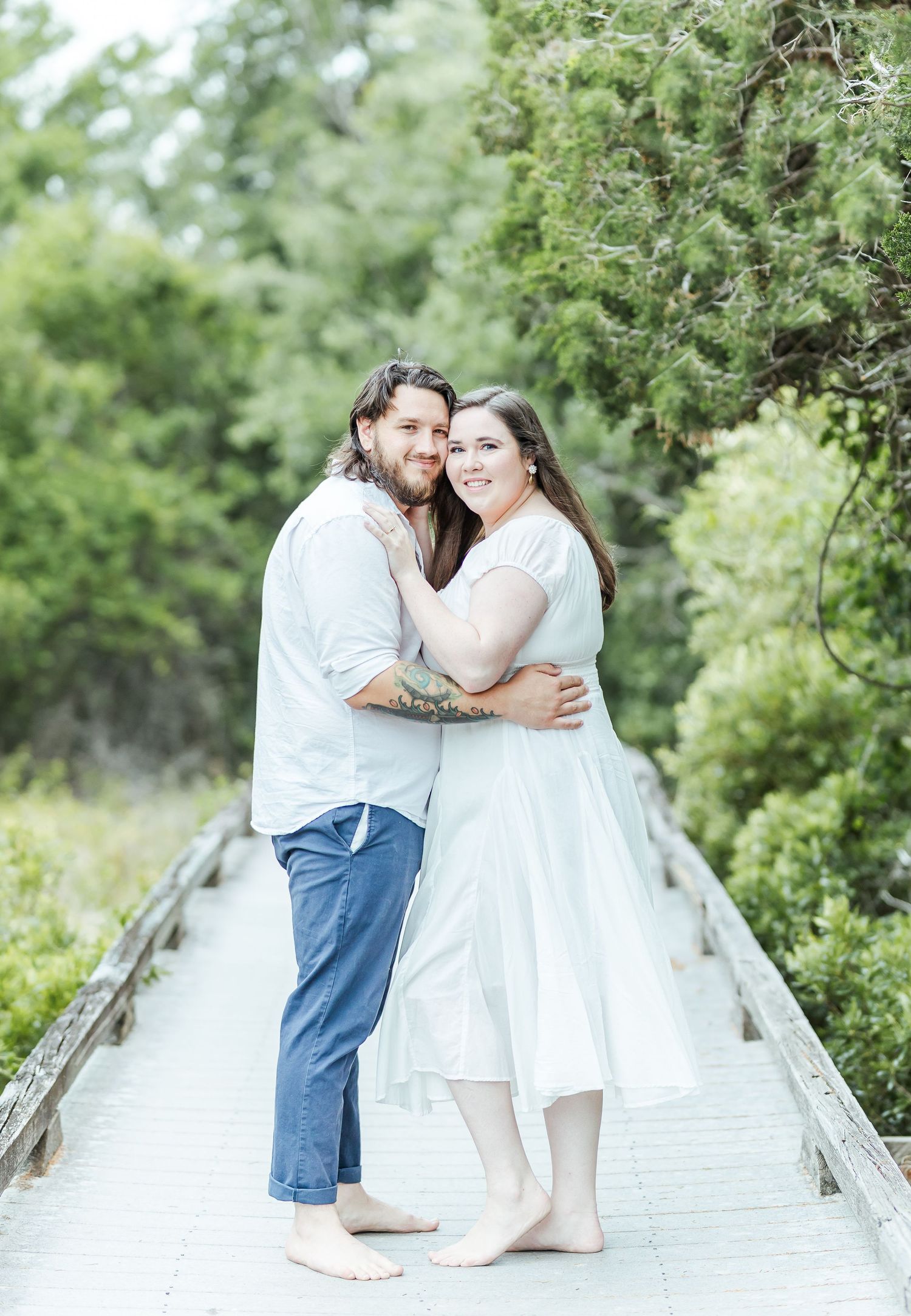 A romantic couple embraces on a wooden boardwalk surrounded by lush greenery.