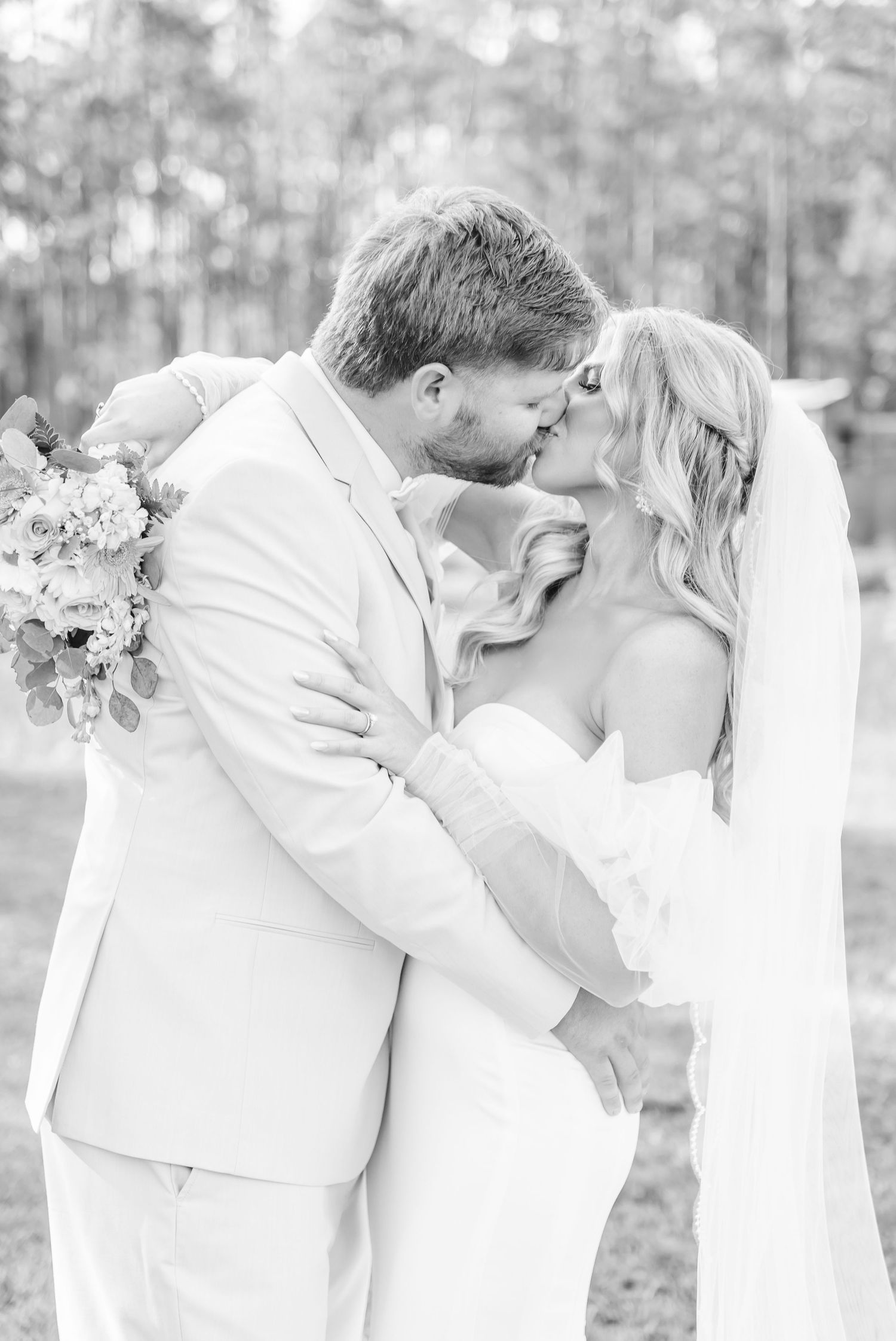 A bride and groom share an intimate kiss during their wedding photoshoot by a lakeside.