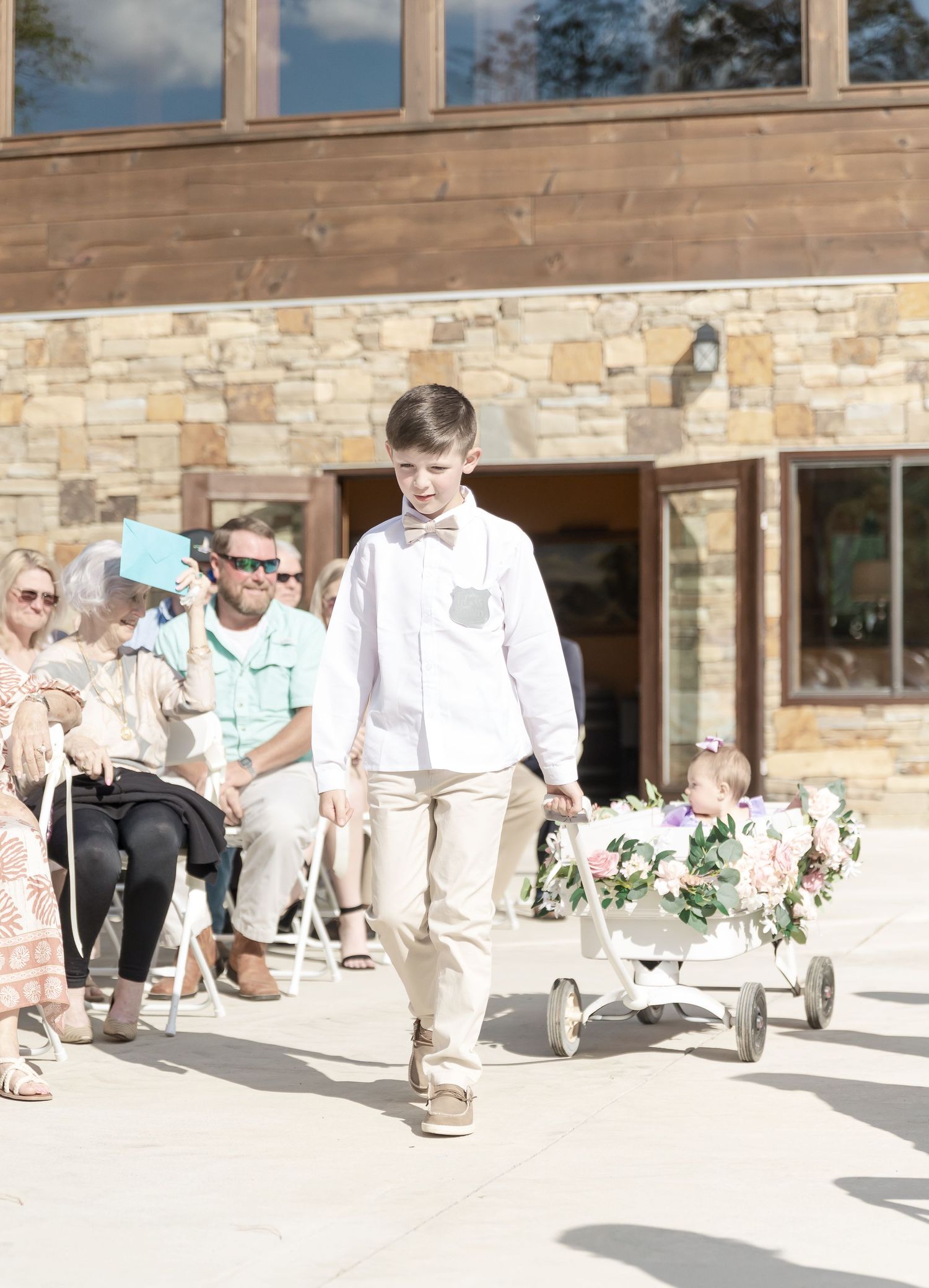 Young attendant pulls decorated wagon down aisle at stone venue wedding.