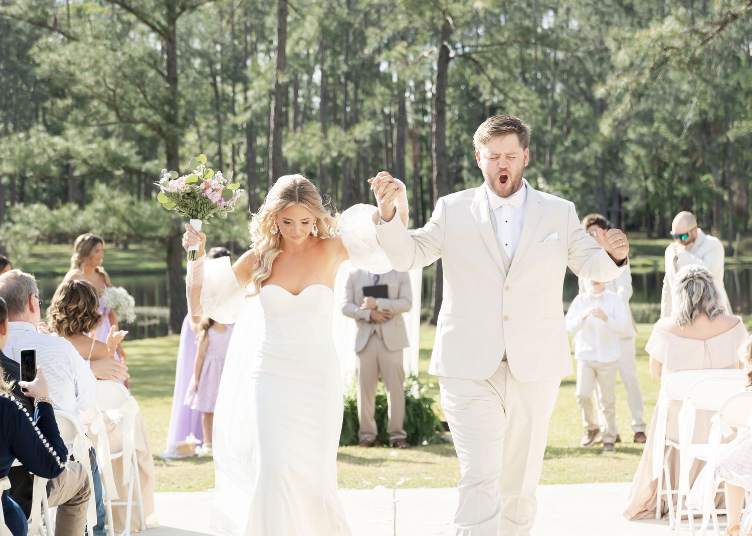 Joyful wedding ceremony exit with guests celebrating in an outdoor pine forest setting.