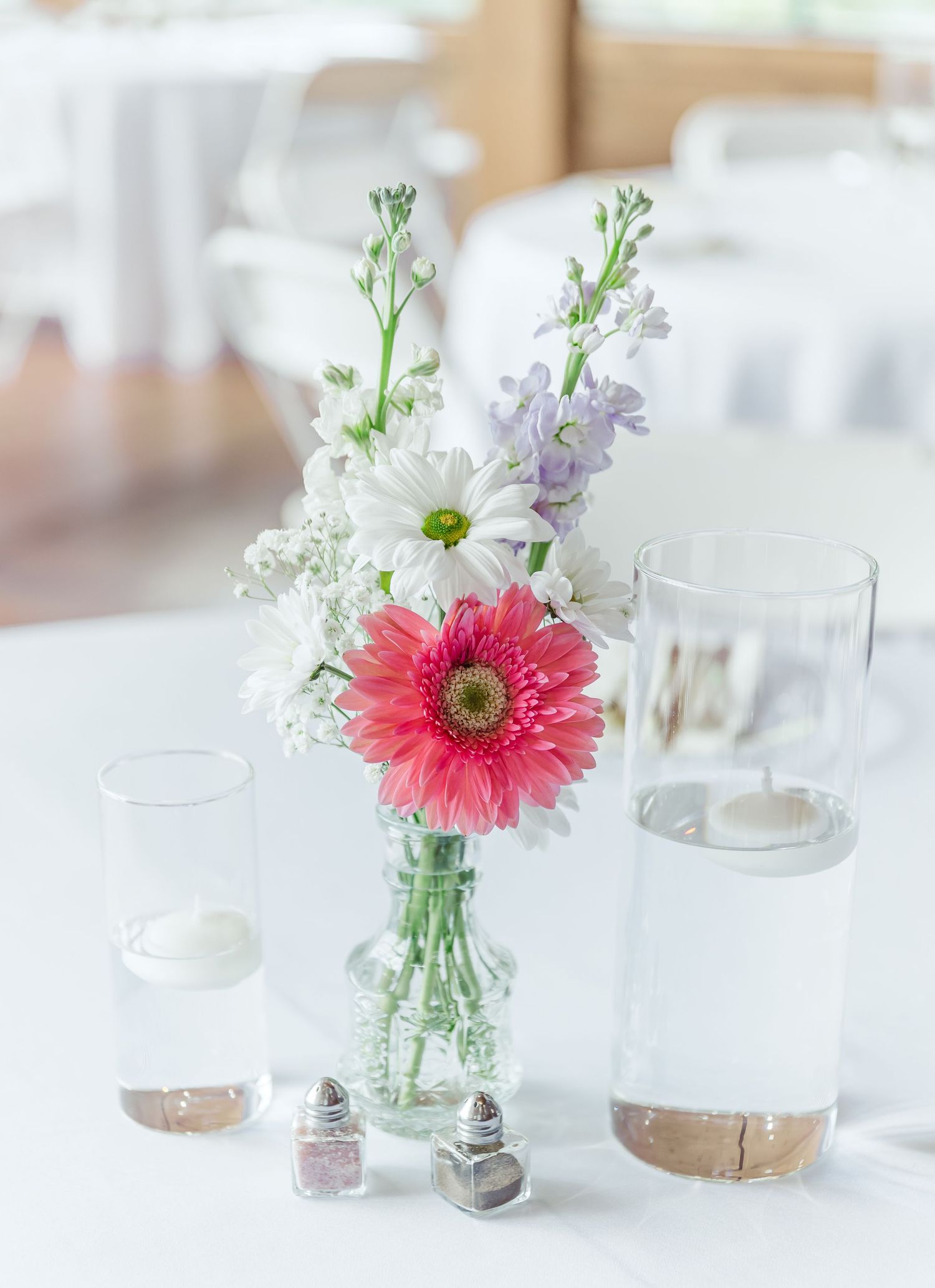 Simple floral centerpiece with pink gerbera daisy and white flowers in glass vase.