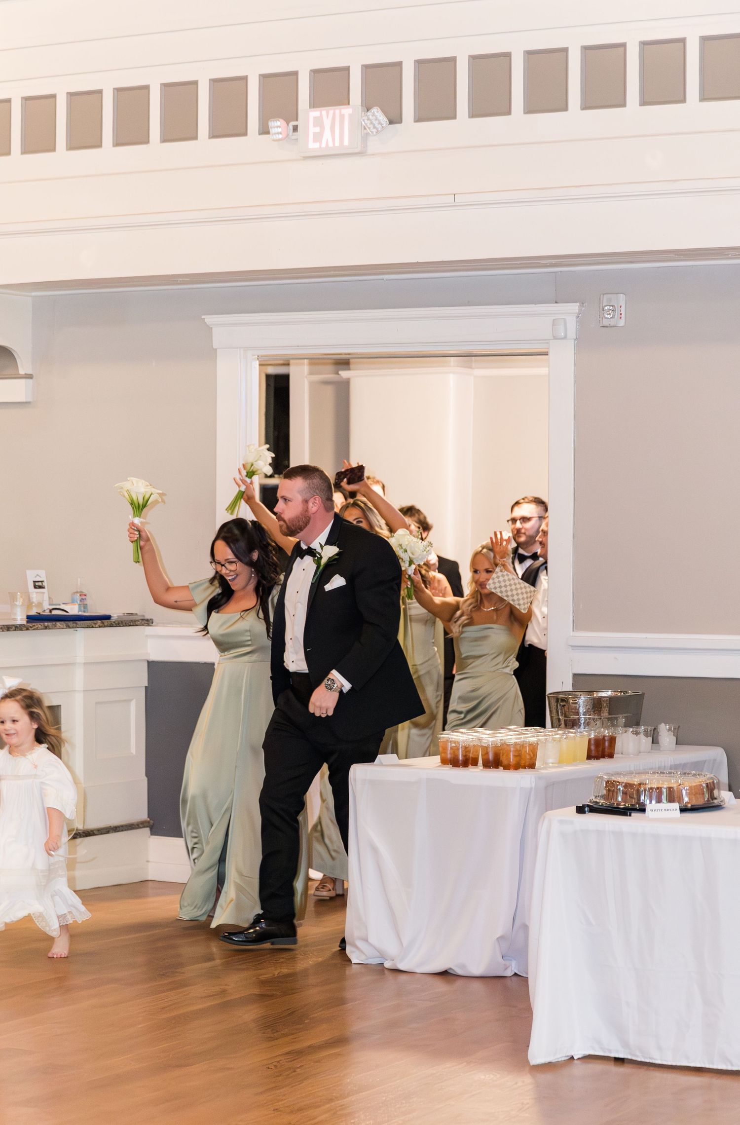 Bride and groom make grand entrance at wedding reception as bridal party cheers behind them.