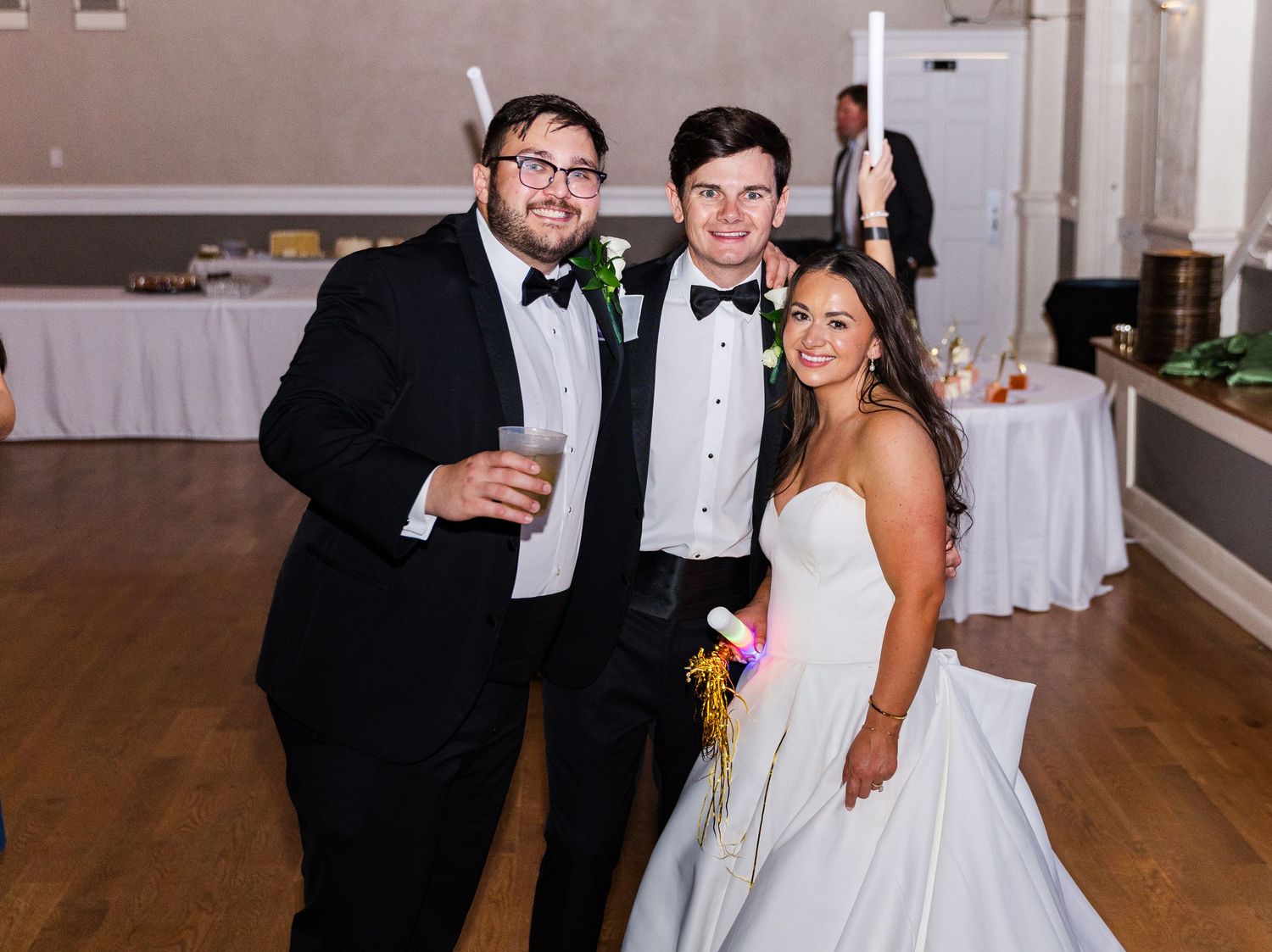 Groom in tuxedo poses with two guests at elegant wedding reception.