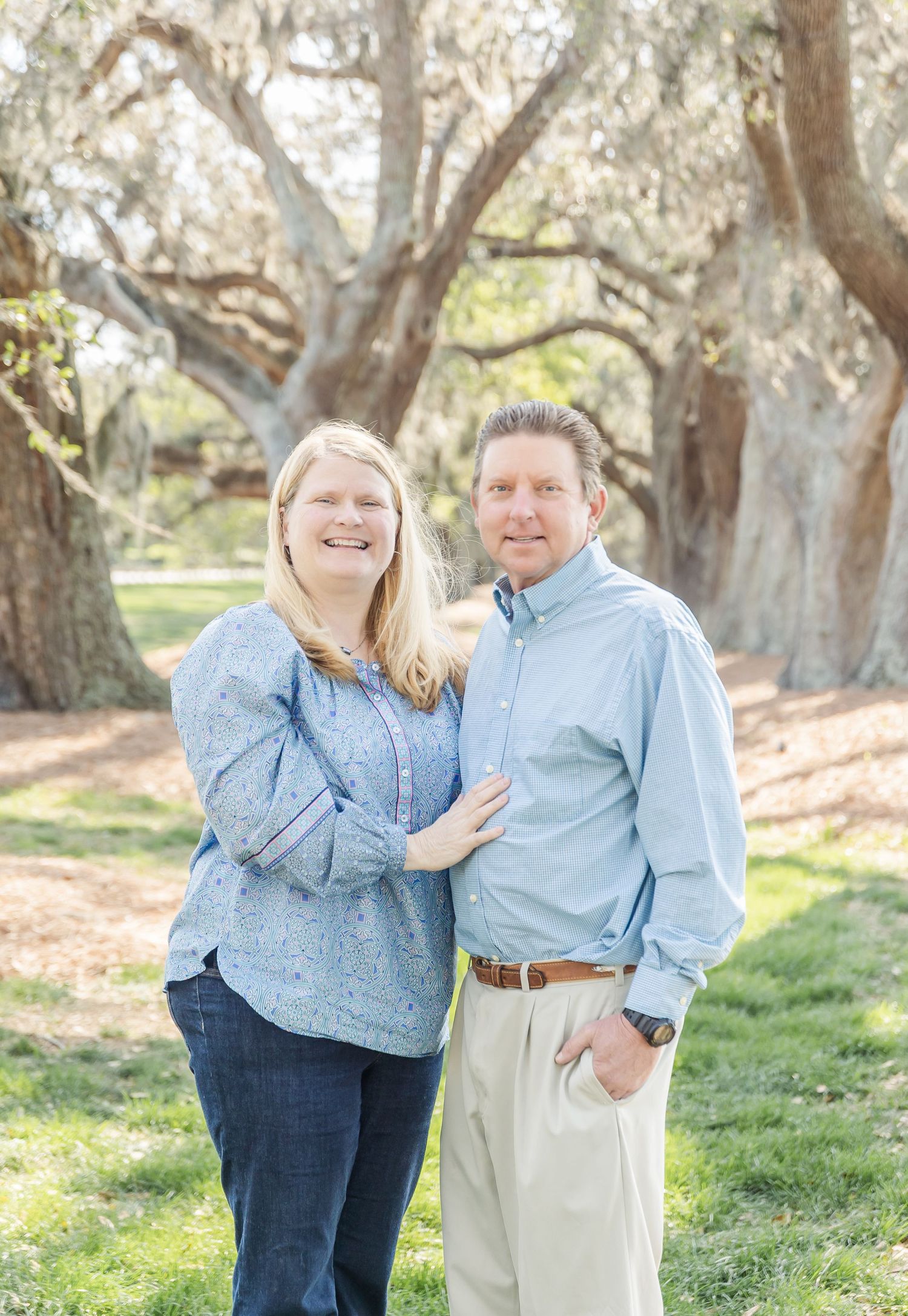 Happy couple in coordinating blue button-downs embraces while standing in a scenic park setting.