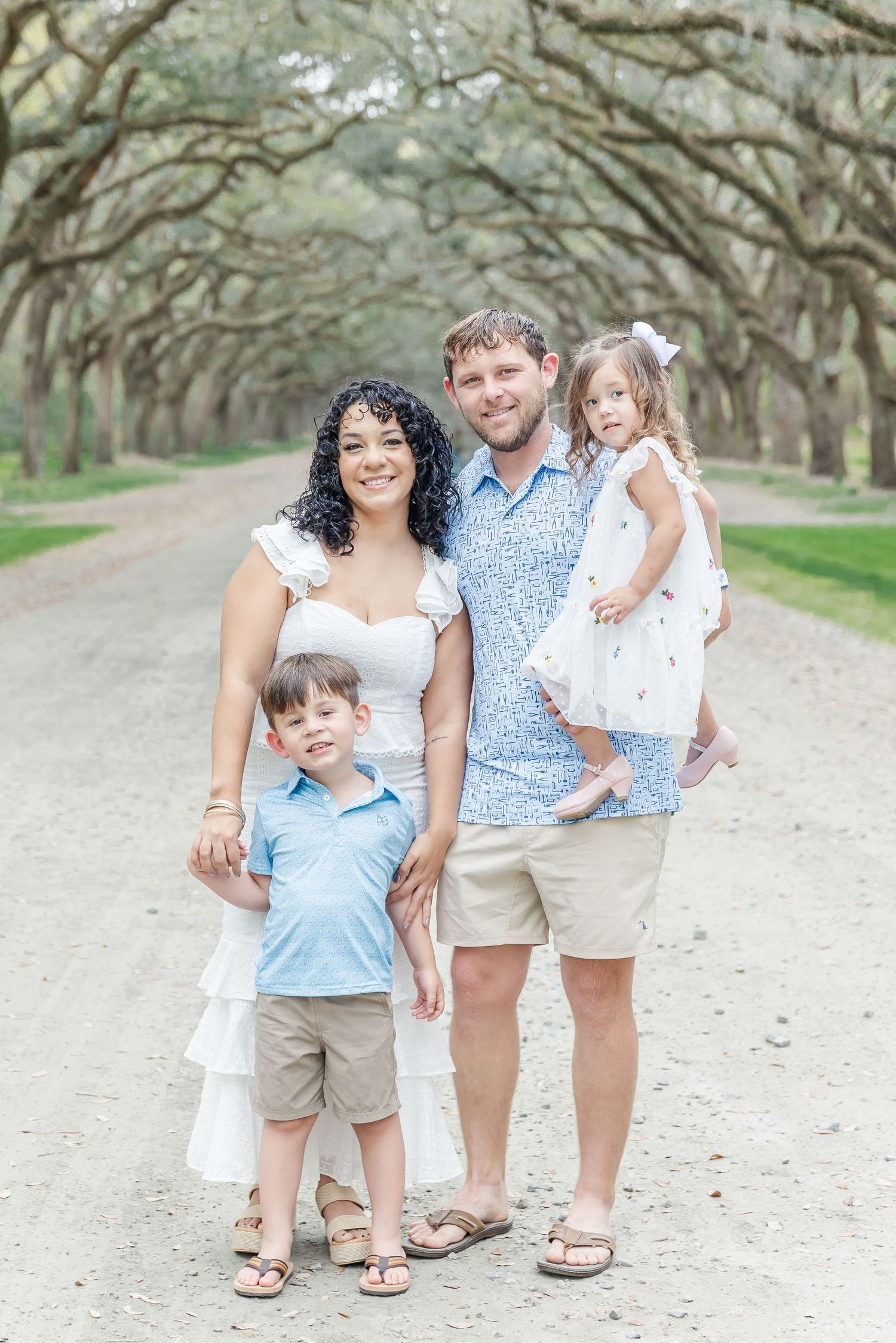 Family portrait on a tree-lined path with arching oak branches creating a natural canopy overhead.