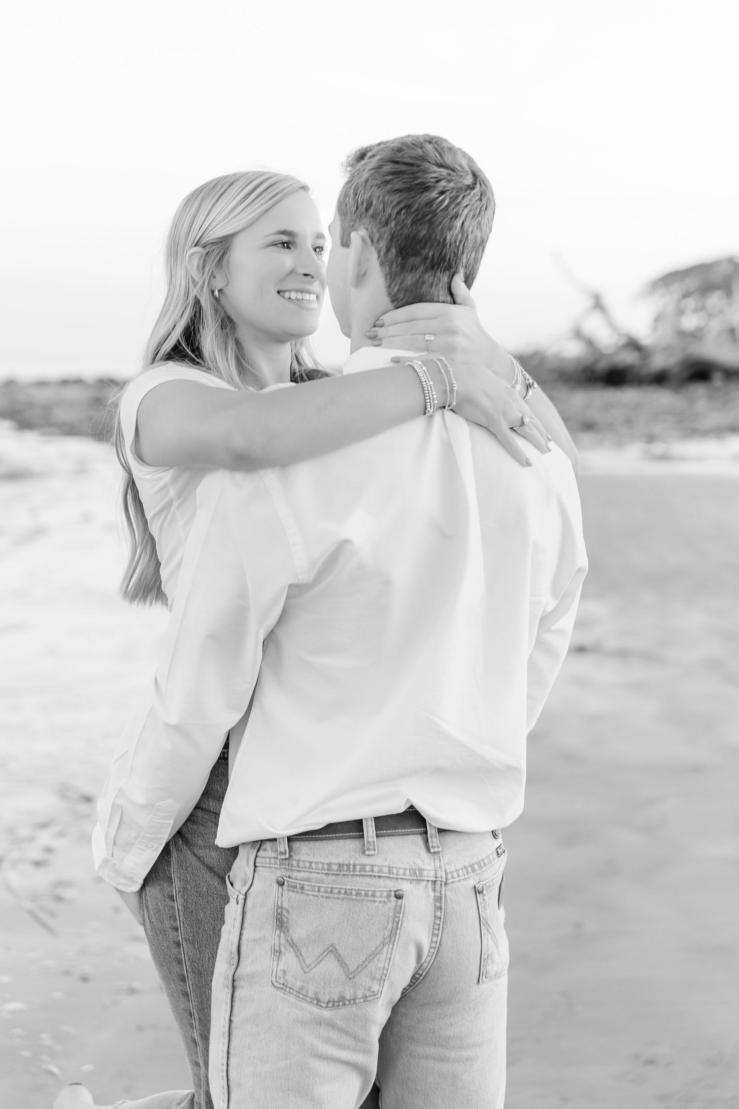 A couple in white shirts and jeans share a loving embrace on a beach.