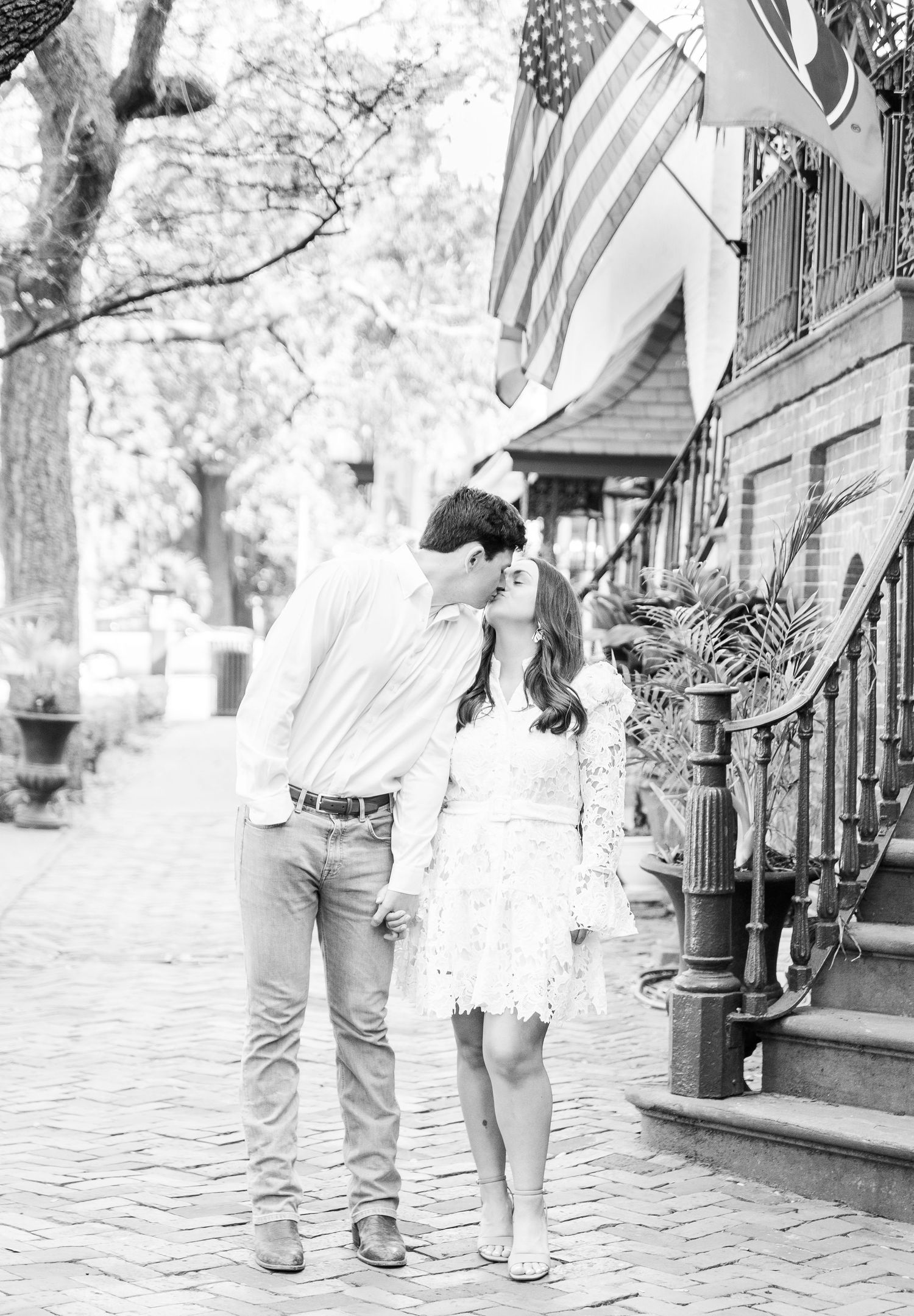 A black and white photo of a couple sharing an intimate moment on a cobblestone street.