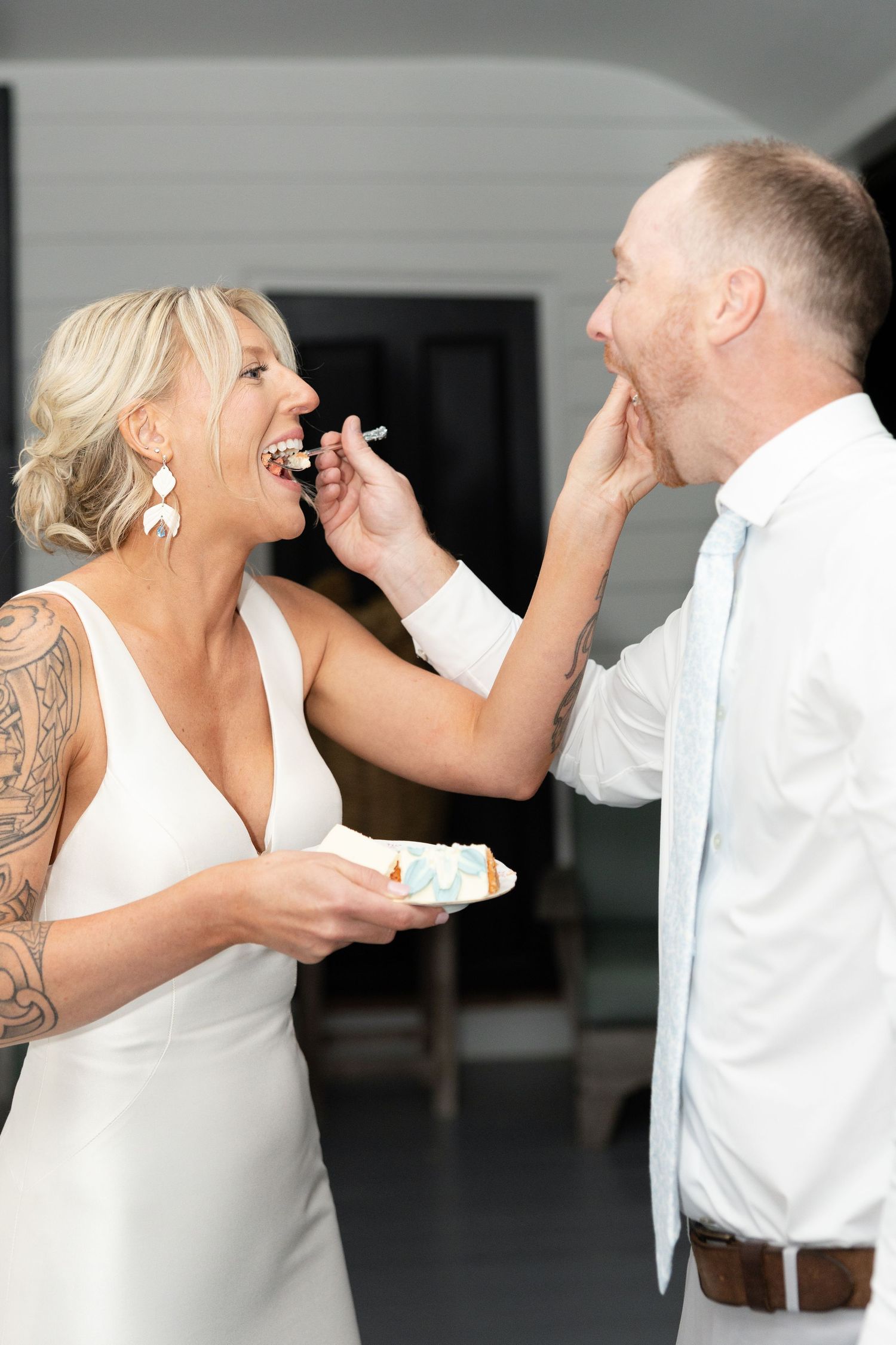 Bride and groom laughing while feeding each other wedding cake at their reception.