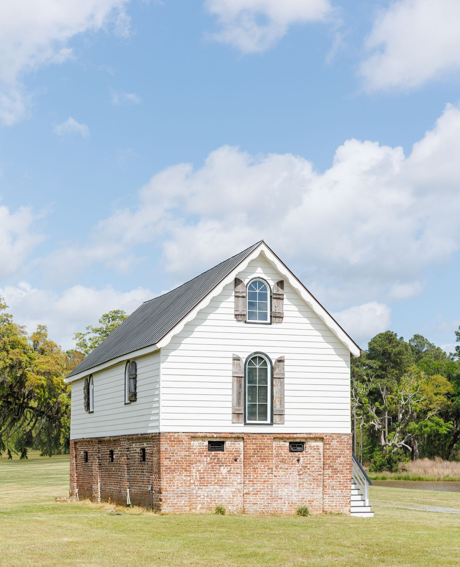 Historic white clapboard chapel with brick foundation under blue sky on green lawn.