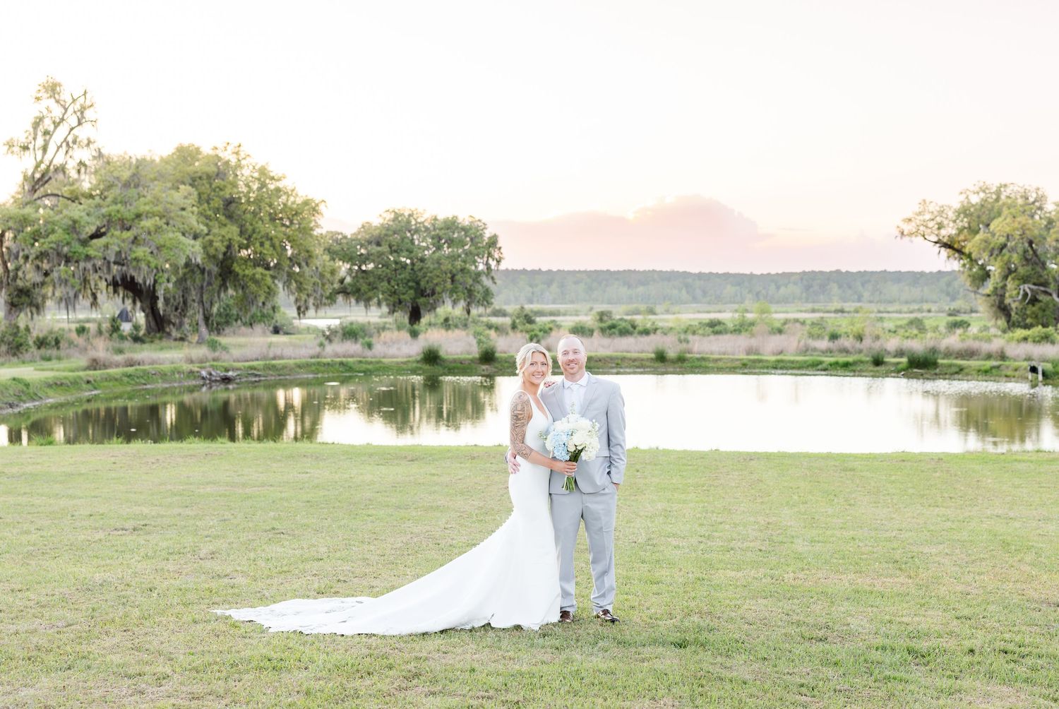 Bride and groom pose romantically by a pond at golden hour with mountain views in the background.