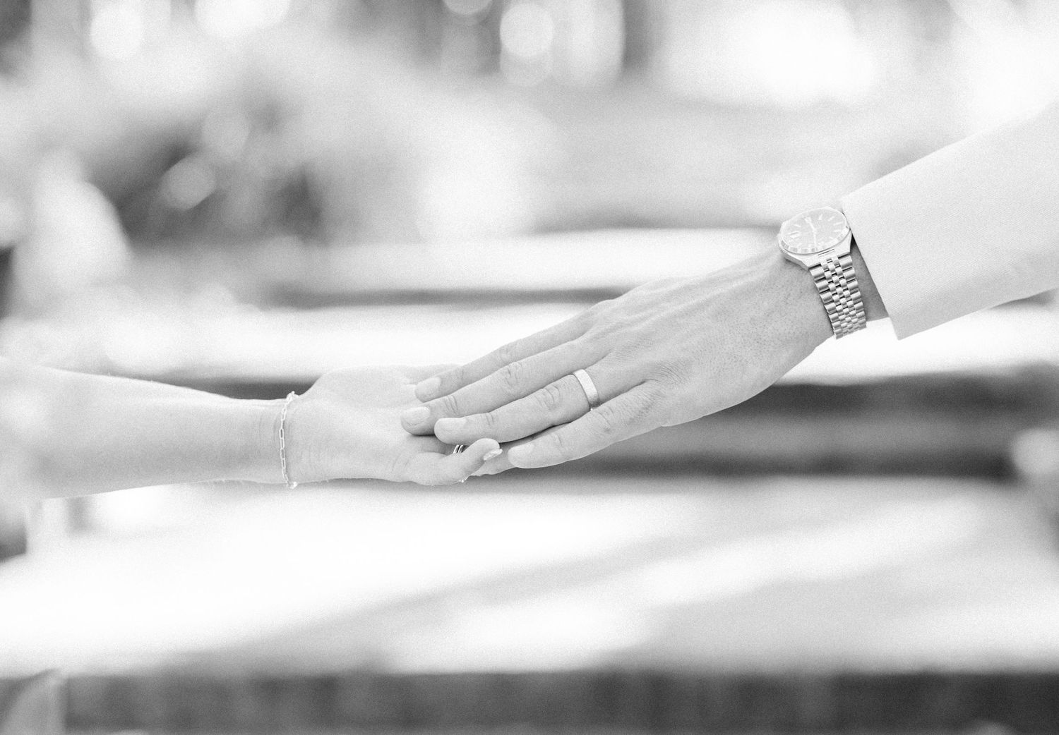 Black and white photo of bride and groom holding hands, groom wearing silver watch and wedding band.