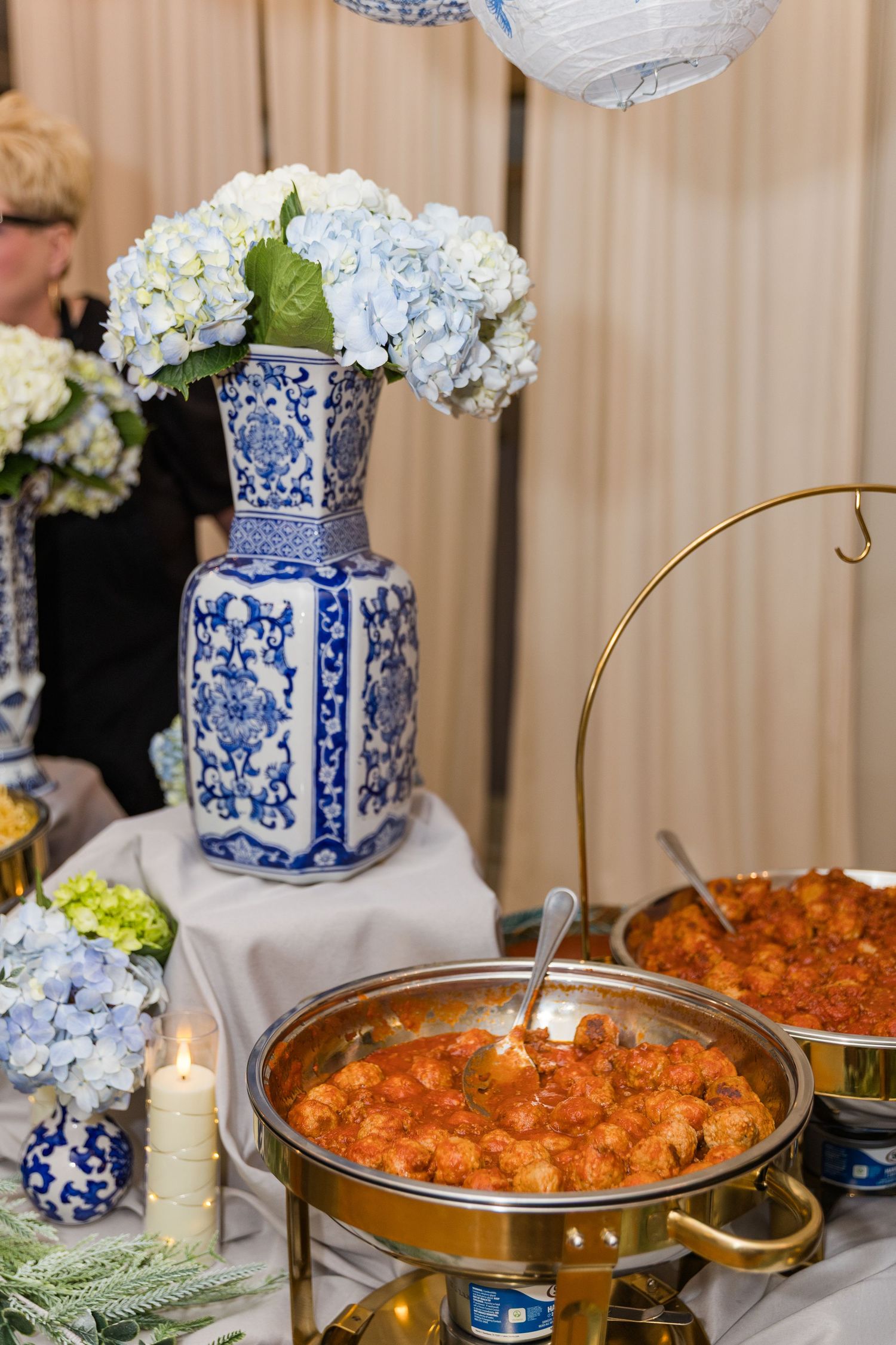 Wedding catering table with shrimp dish in gold chafing dish and blue hydrangeas in chinoiserie vase.