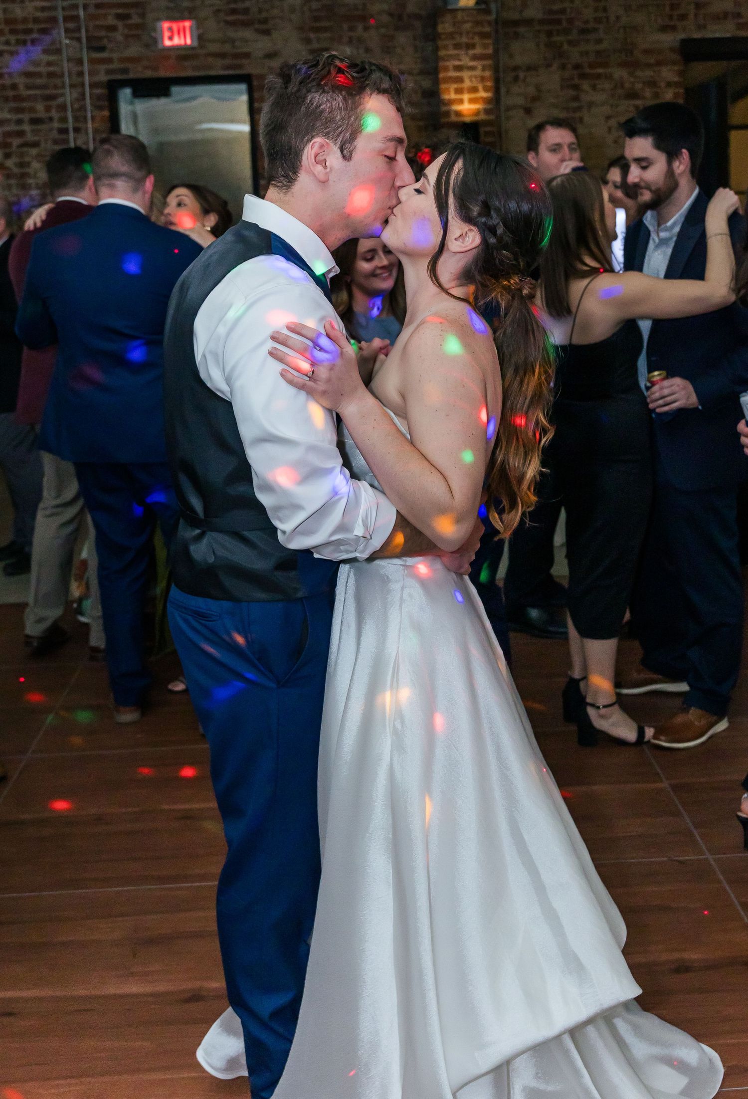 A couple shares a romantic dance moment at their wedding reception with disco lights casting colorful reflections.