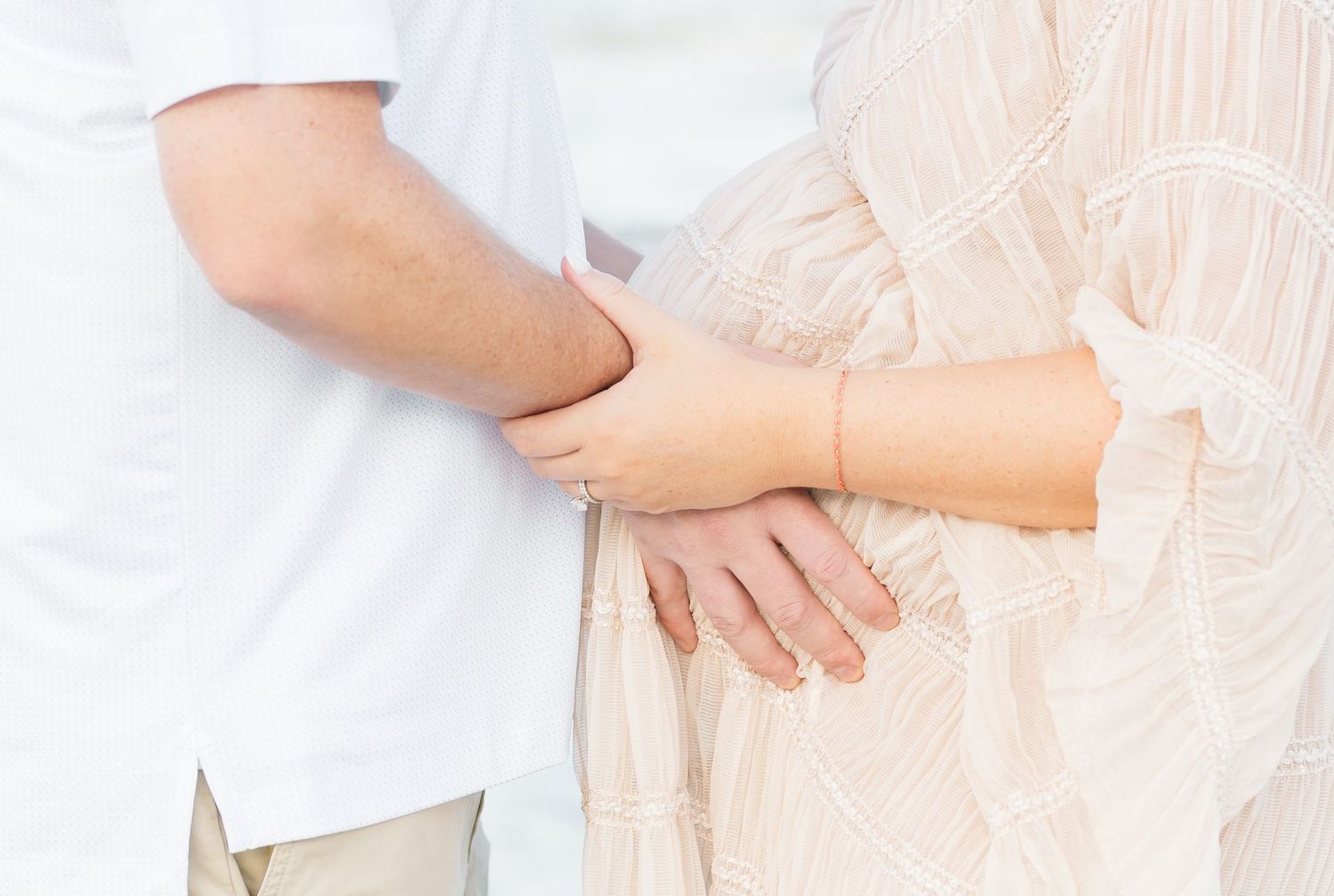 Close-up of hands resting on a pregnant belly in delicate beige fabric.