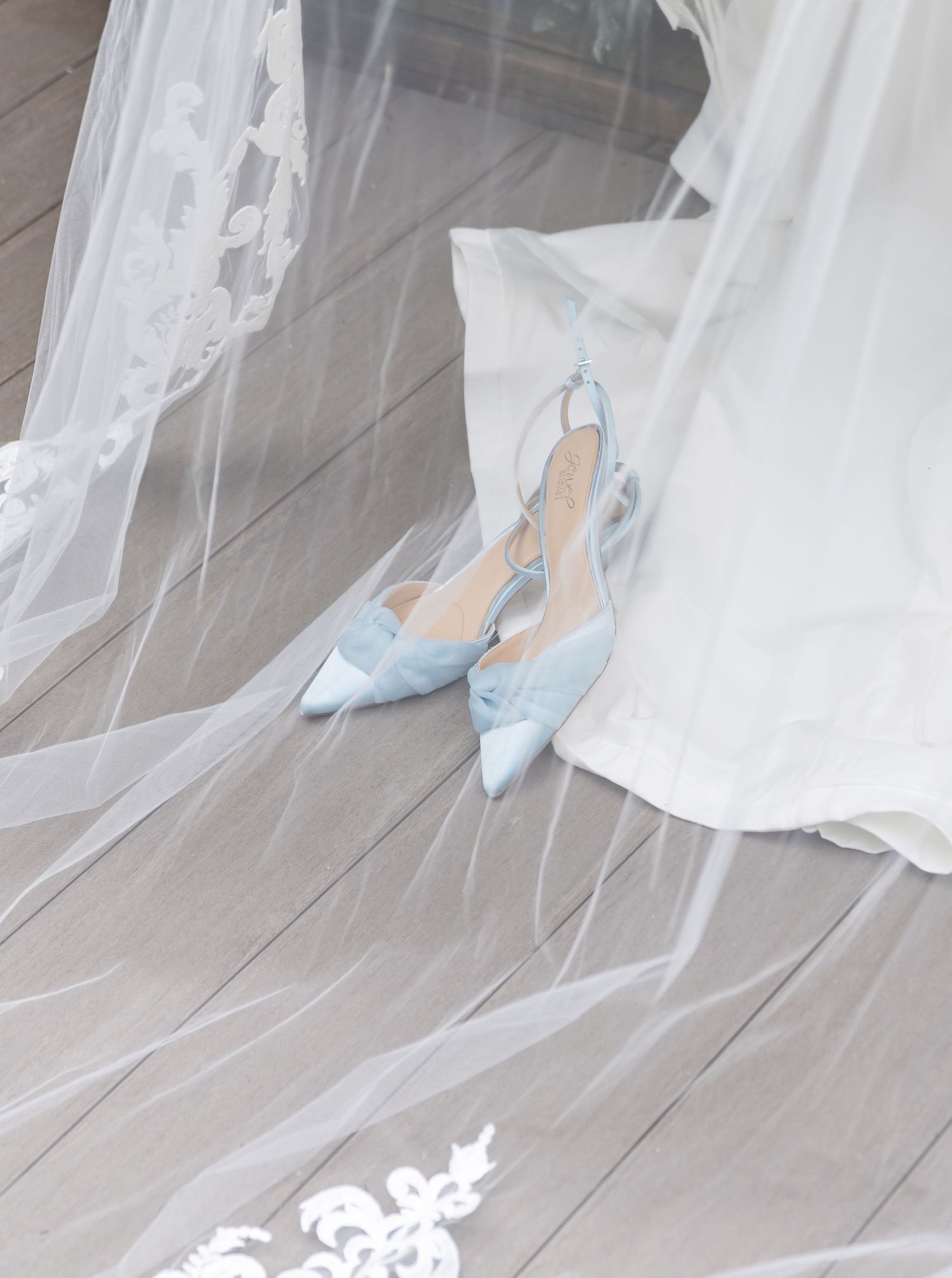 White wedding veil drapes elegantly over pale blue bridal shoes on a light wooden floor.