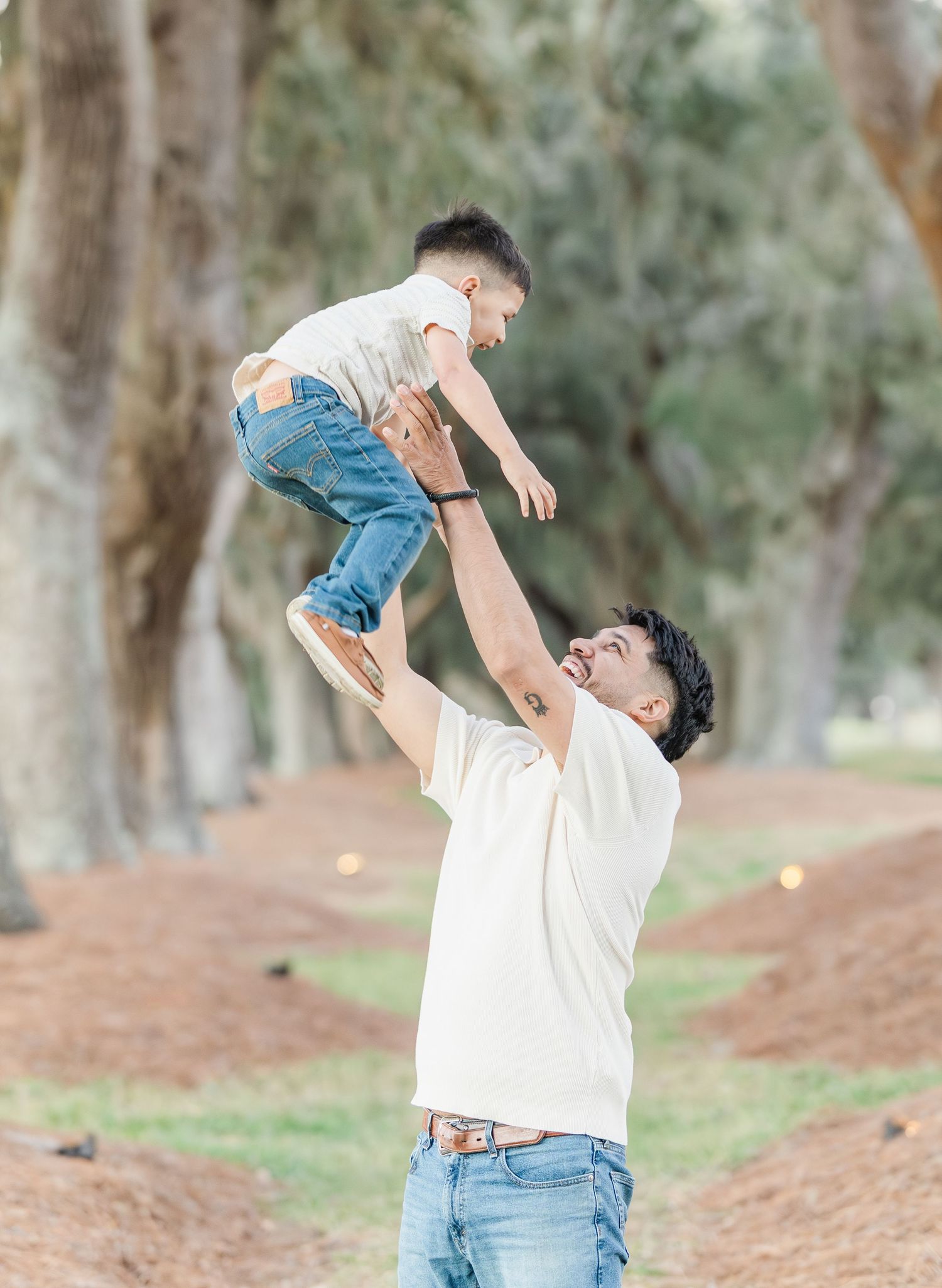 Parent lifting and playing with small child in joyful moment outdoors.
