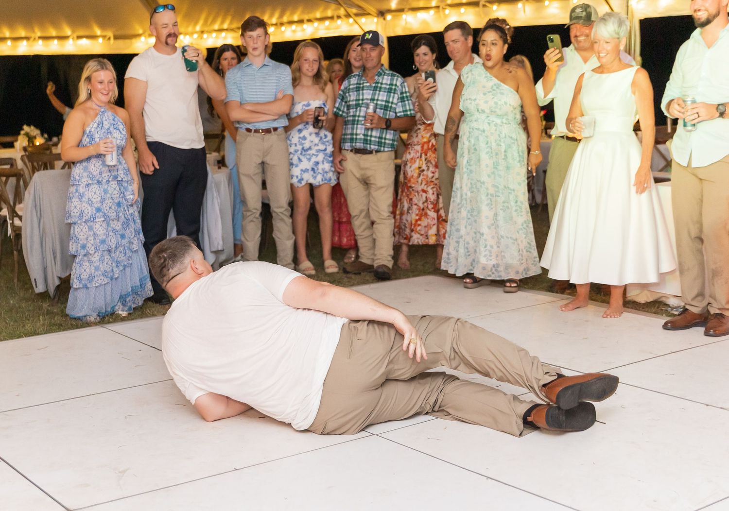 People dancing at a wedding reception on a white dance floor under warm lighting.