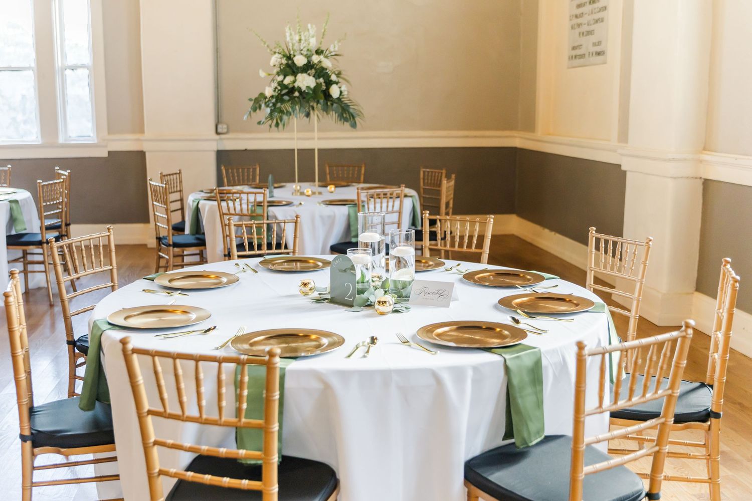 Wedding reception venue with round tables set with white linens and wooden chiavari chairs.