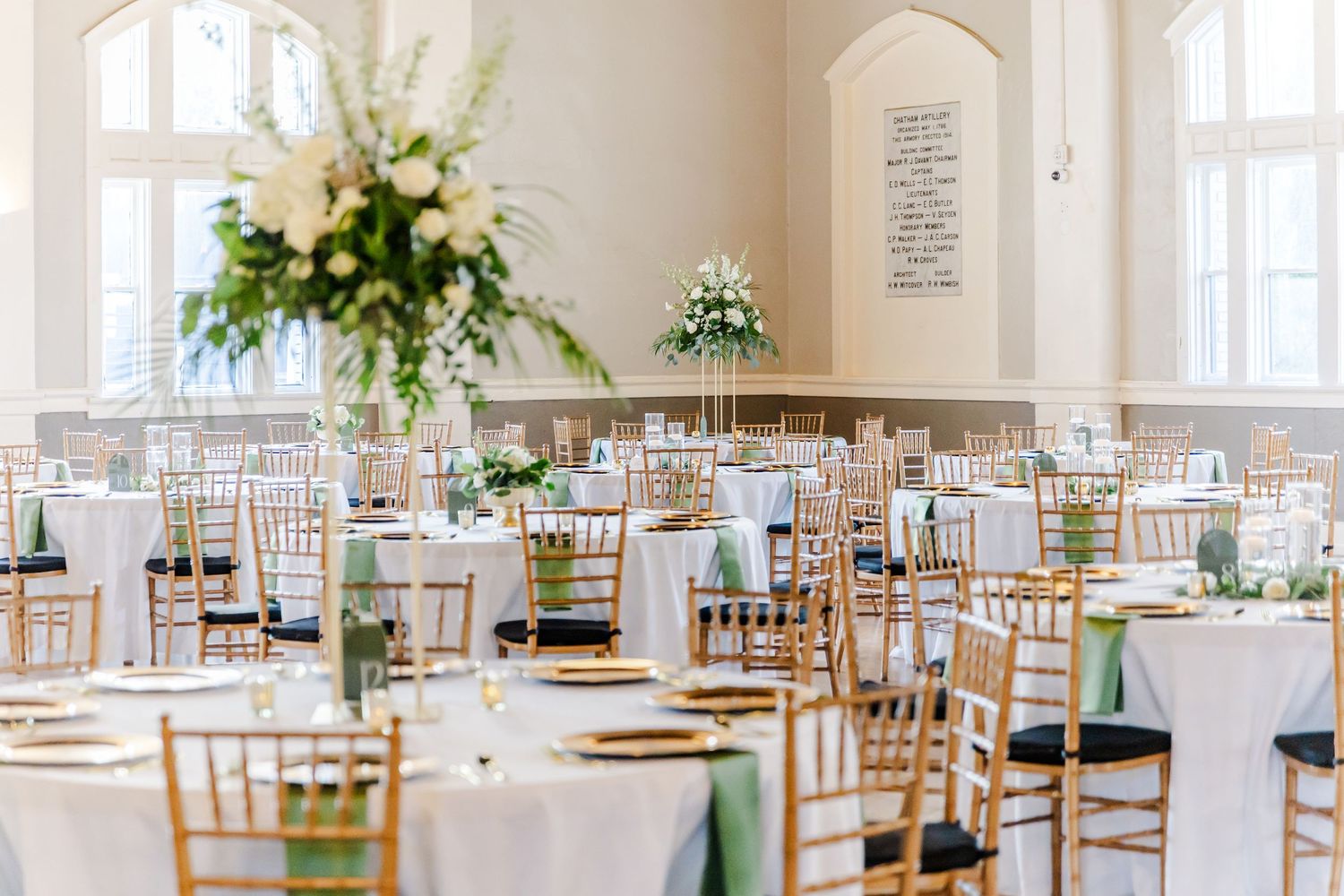 Bright white wedding reception venue with wooden chairs and elegant floral centerpieces.