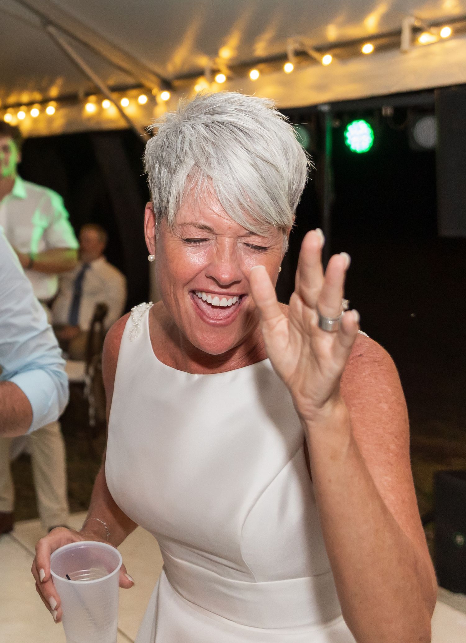 Wedding guest in white dress laughing joyfully during reception celebrations.