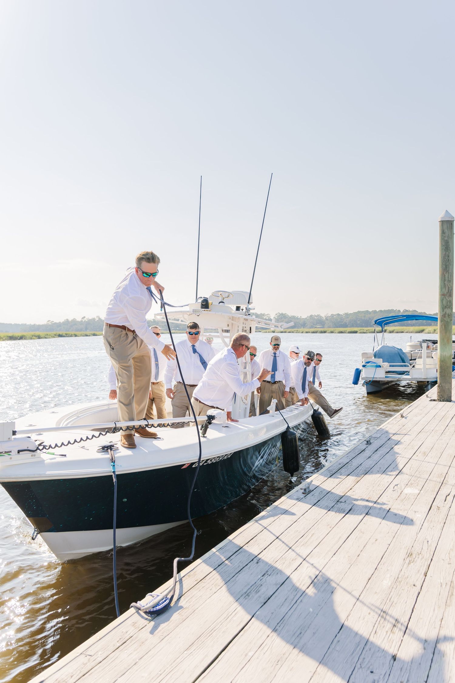 Group in white attire boarding boats at a wooden dock on a sunny afternoon.