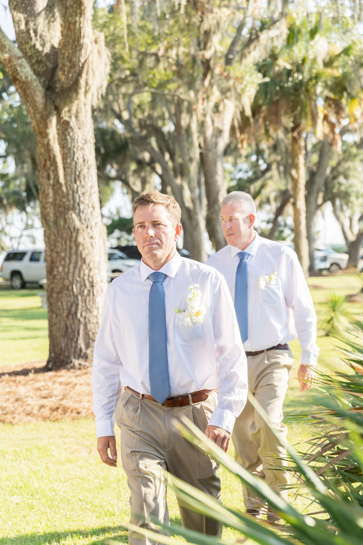 Two people walk through a lush garden path with Spanish moss hanging from oak trees overhead.