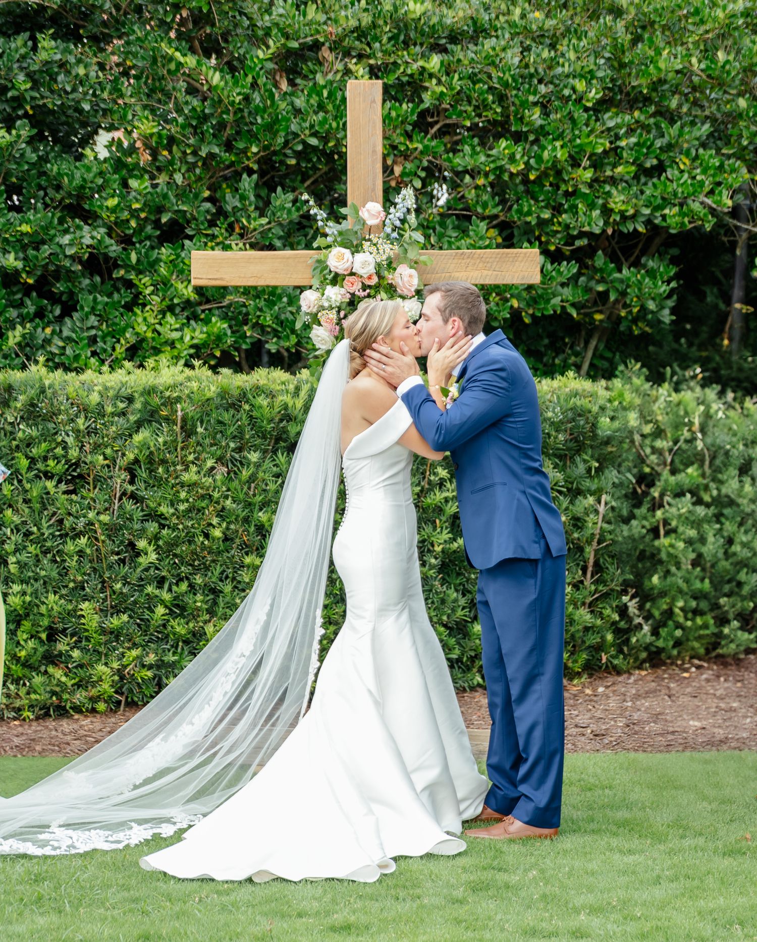 Couple in wedding attire sharing a romantic kiss sequence in a lush garden setting with flowing veil and navy suit.