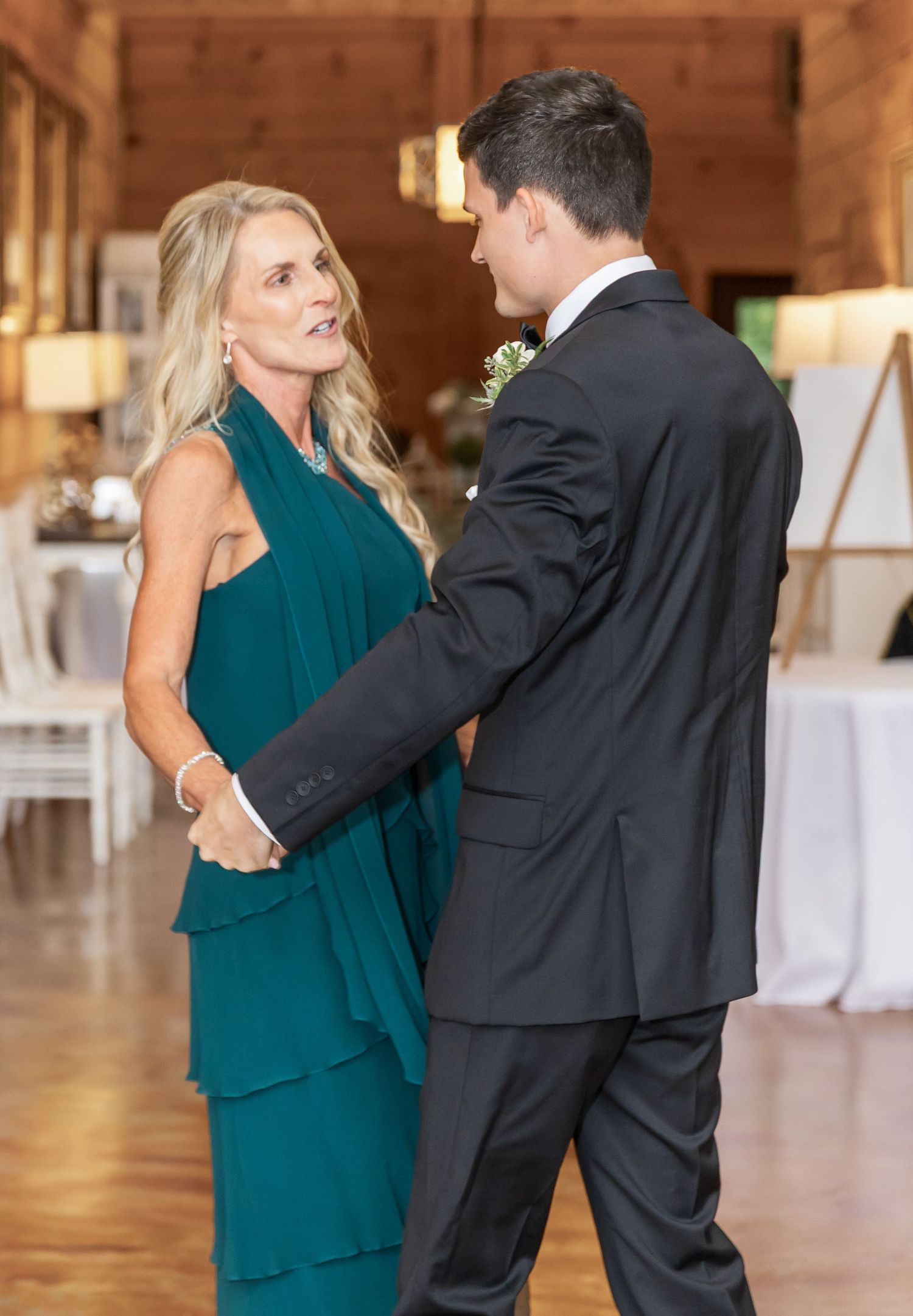Dancers in teal and black formal wear move gracefully across a wooden floor at an event.