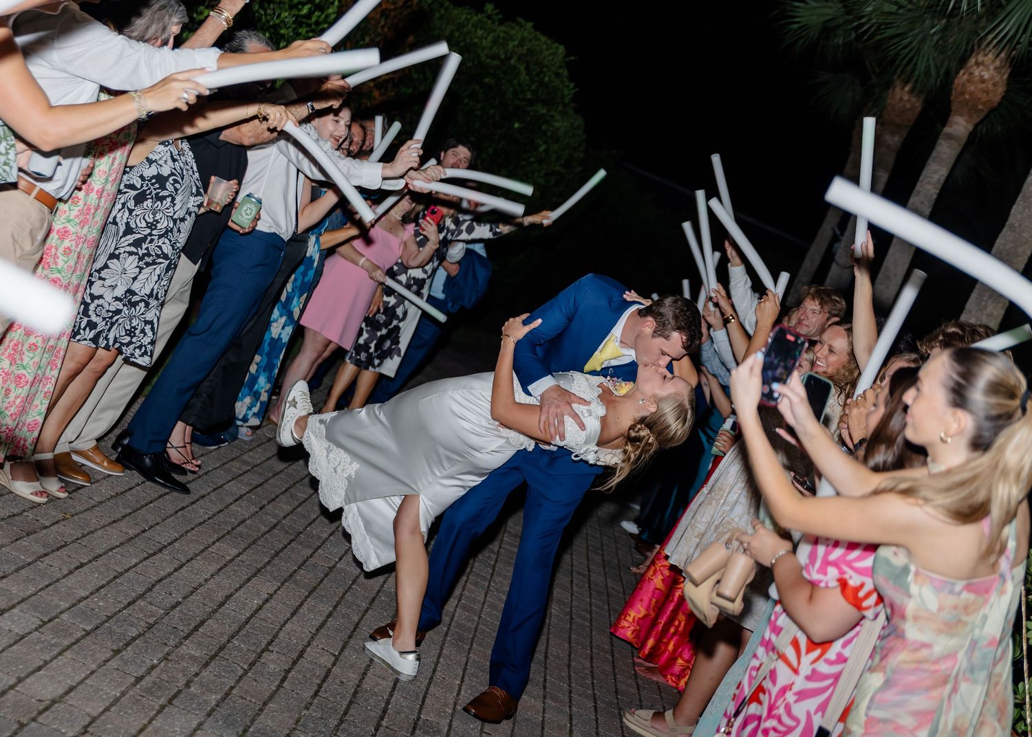 Wedding guests dance and lean back dramatically on a wooden deck during a lively reception celebration.